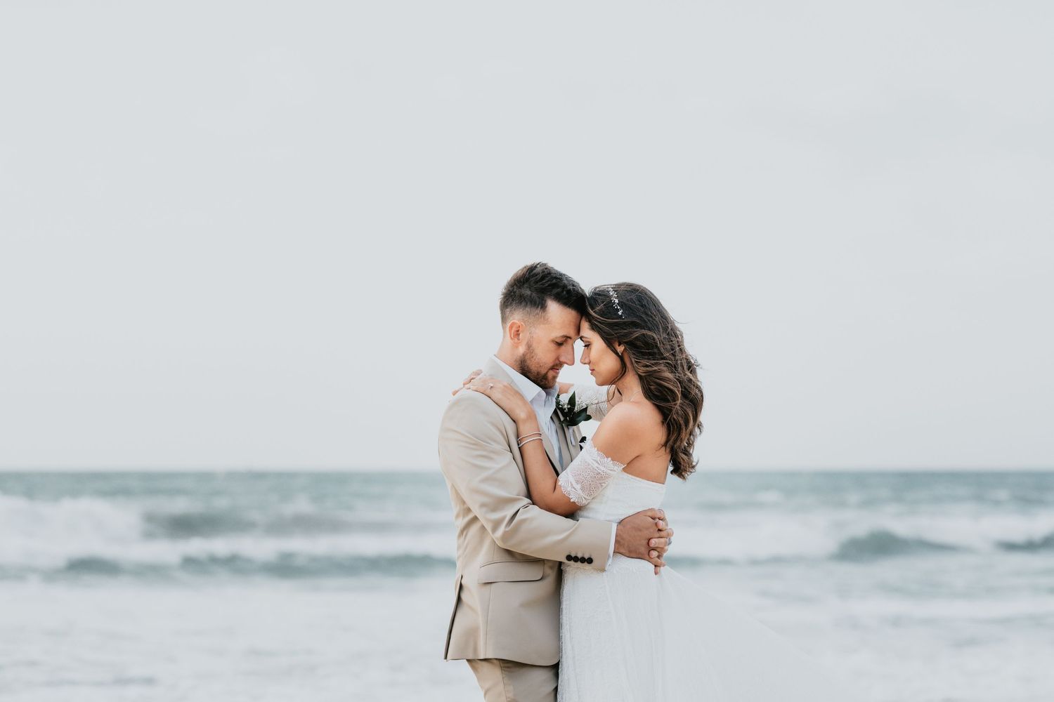 Couple embracing during sunset beach wedding photos with ocean waves in background.