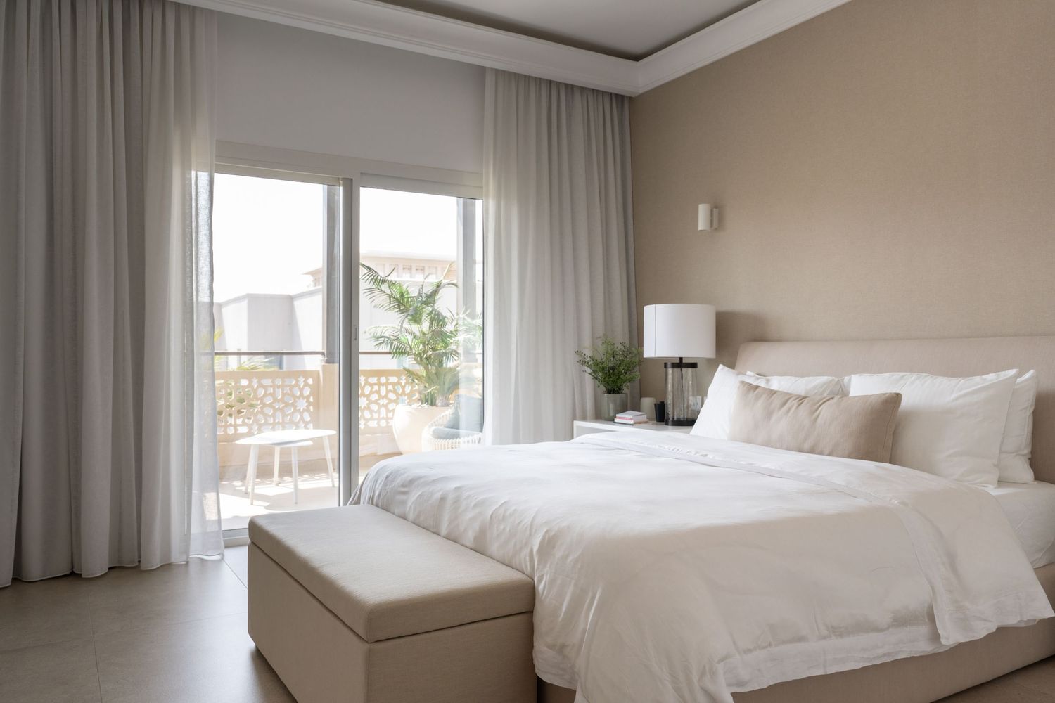 Elegant bedroom with floor-to-ceiling windows, white bedding, and flowing gray curtains.