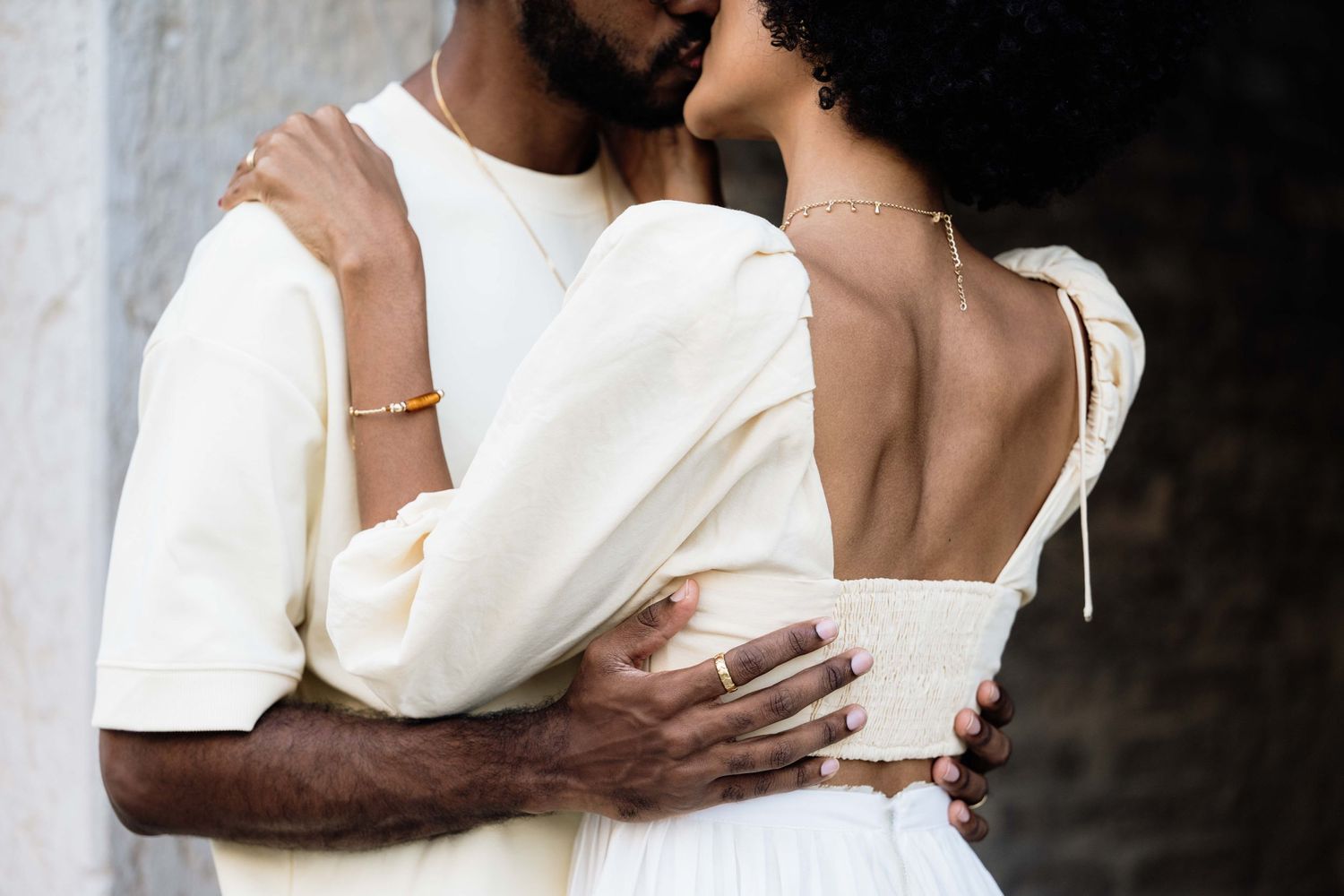 Tender embrace between couple wearing white outfits against dark background.