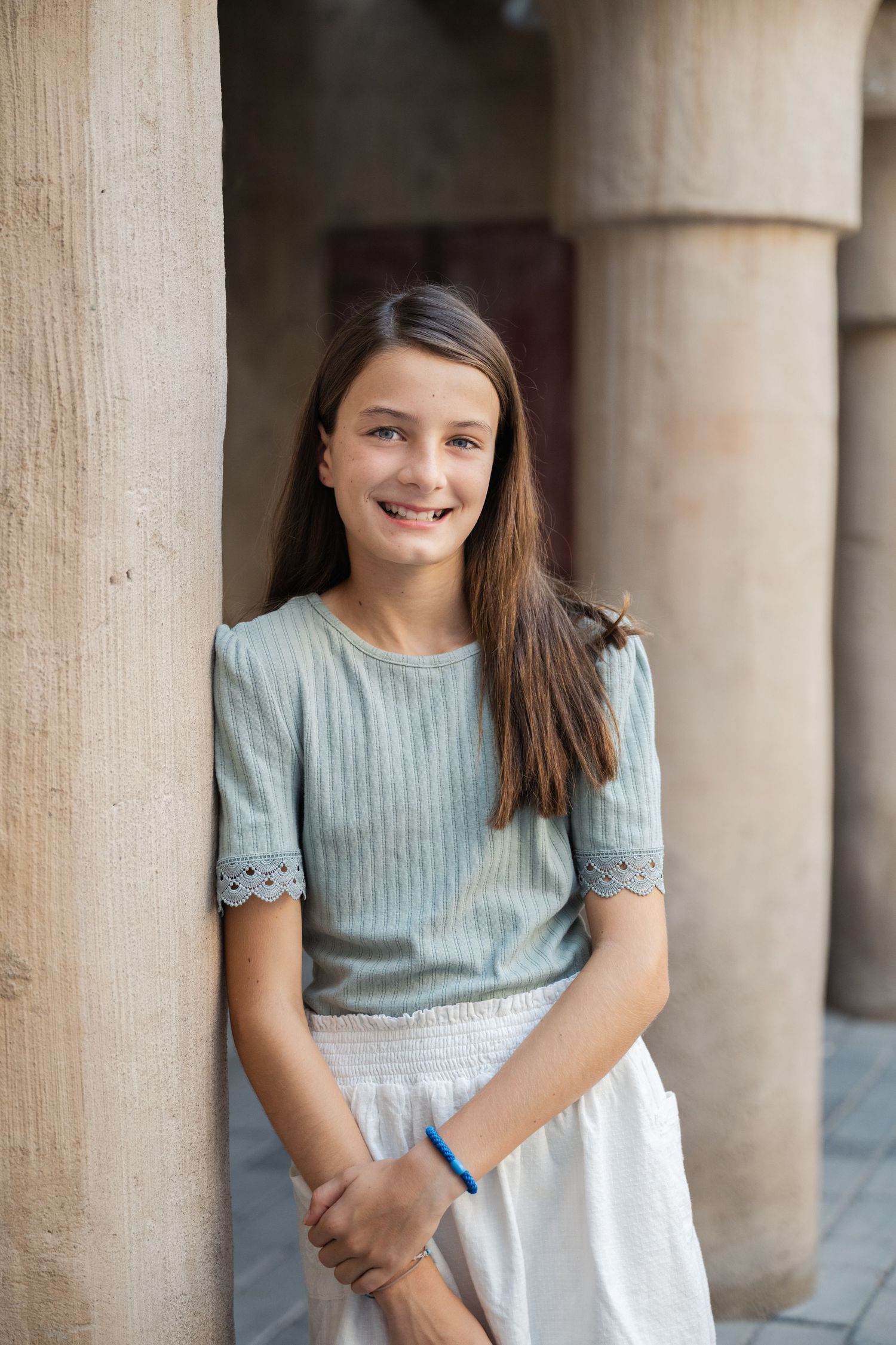 Child in mint green dress posing between stone columns.