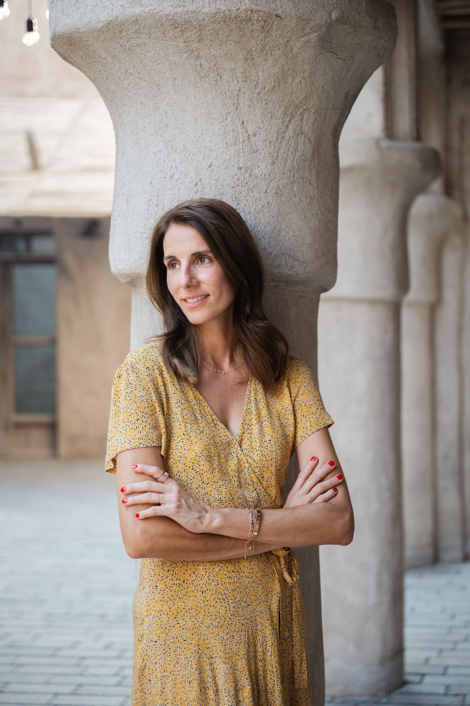 Woman in yellow dress poses confidently against stone pillars in natural light.