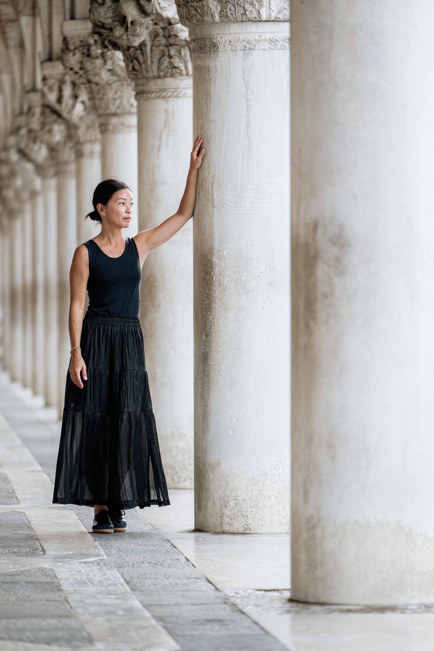 Person in black dress moving gracefully through historic columned arcade.