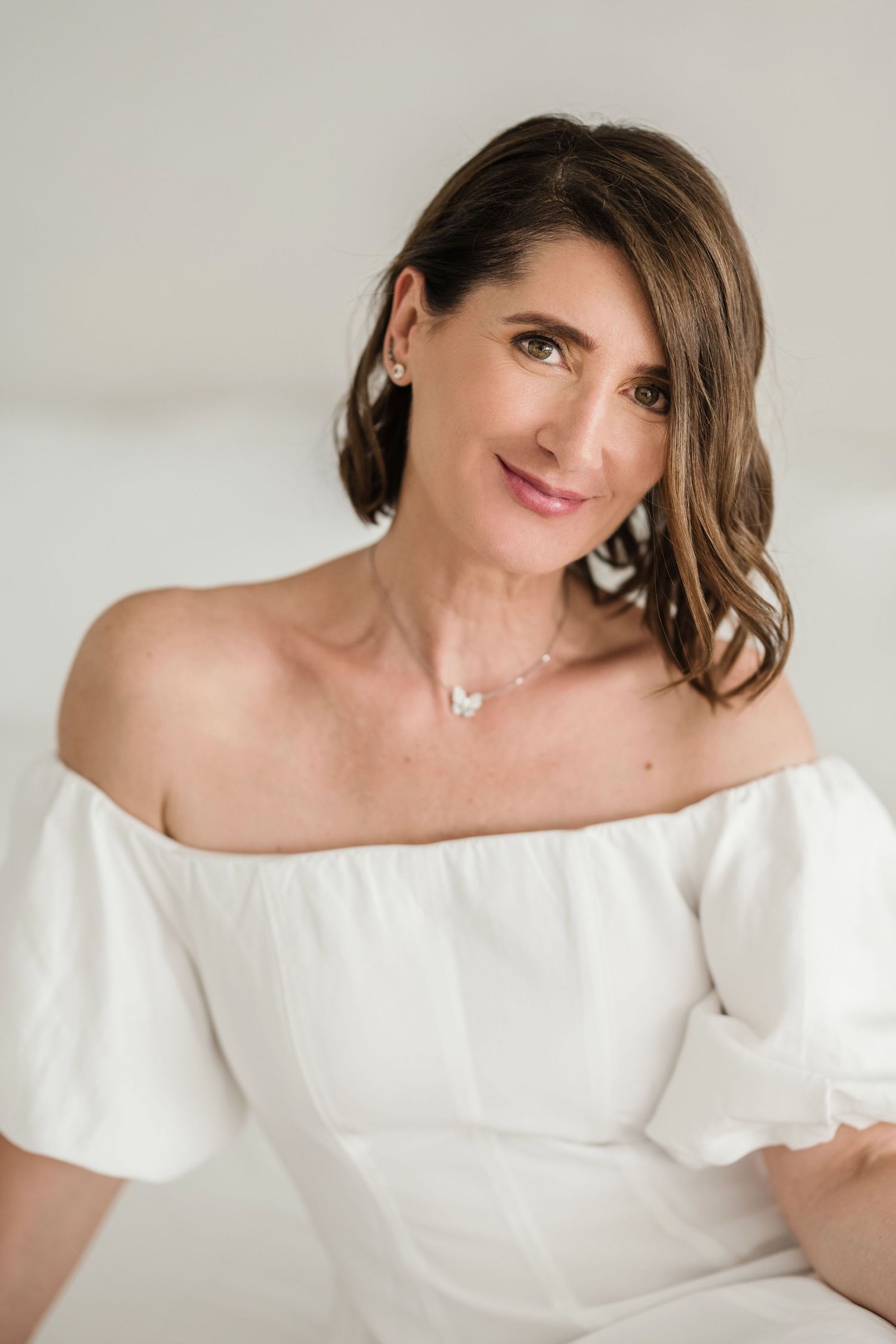 Portrait series showing woman in elegant white off-shoulder top against light background.