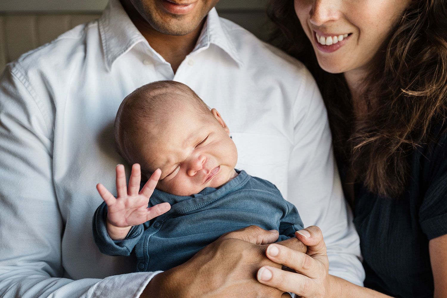 Newborn baby yawning while being held by parents captured in dramatic light