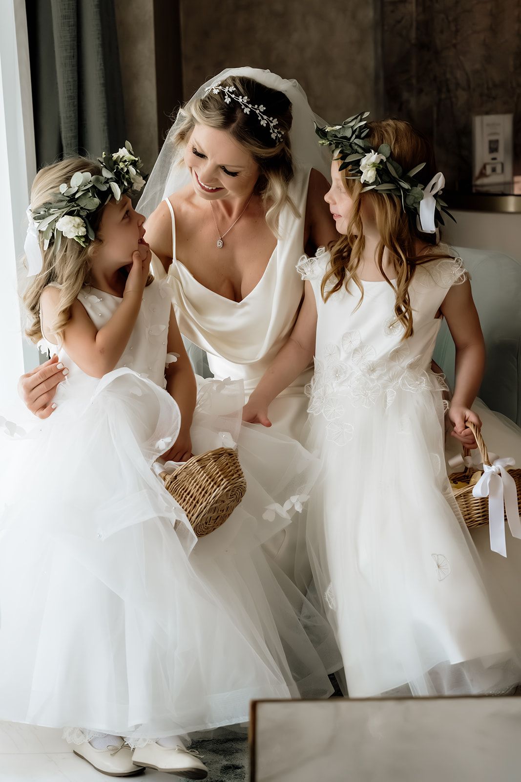 Young attendants in white dresses sharing a sweet moment during wedding preparations.