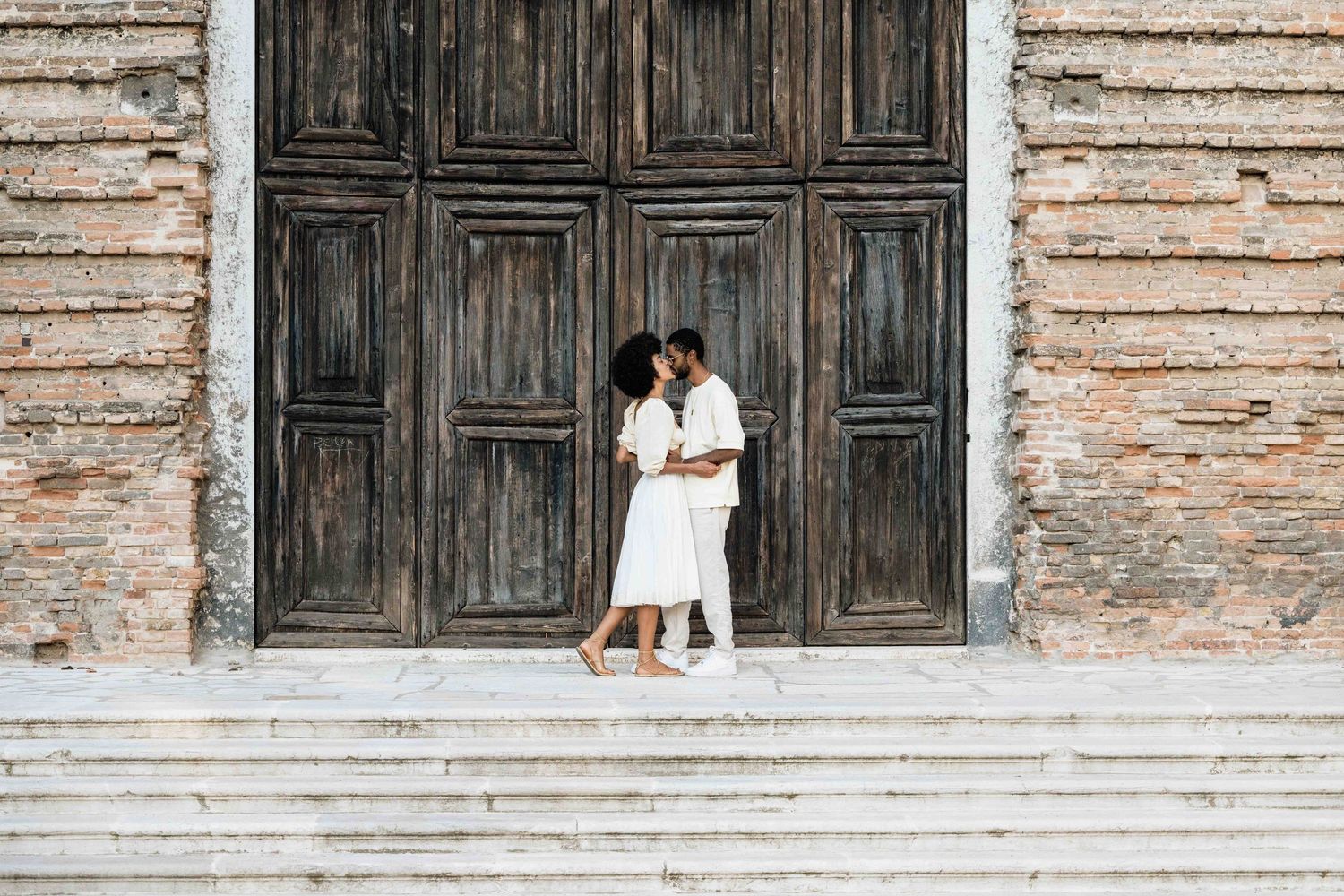 A romantic moment between a couple standing on stone steps by a vintage door.