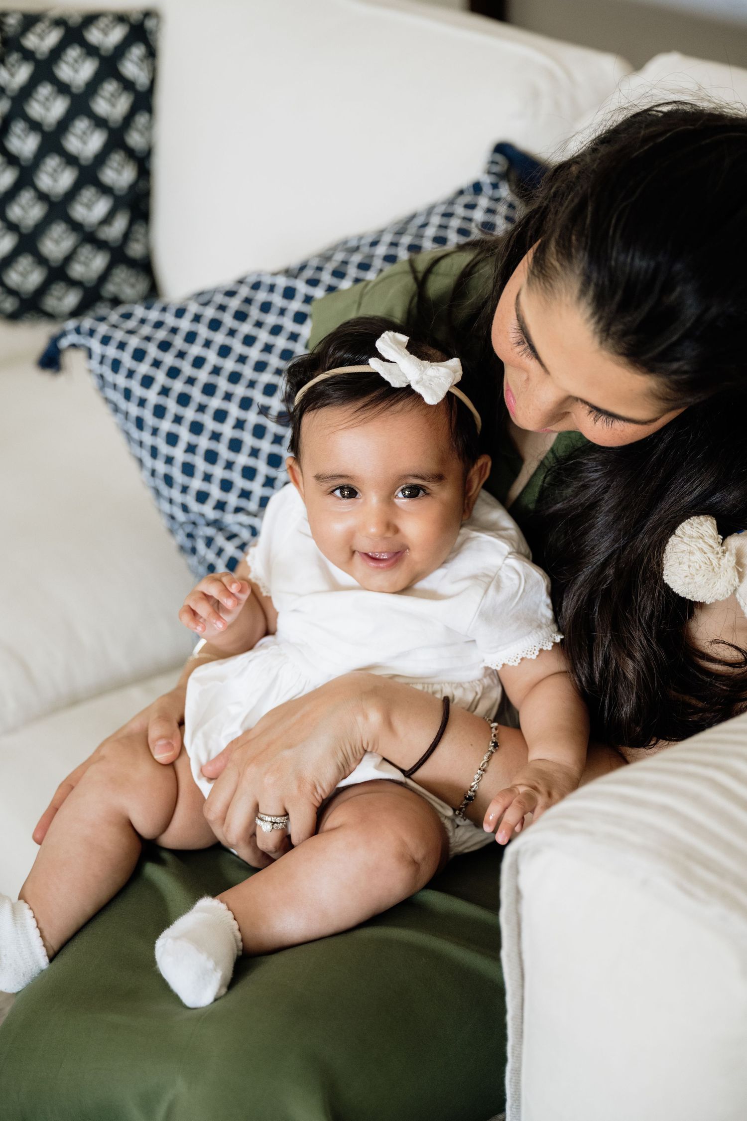 Mother and baby sharing tender moment on white couch with patterned pillows.