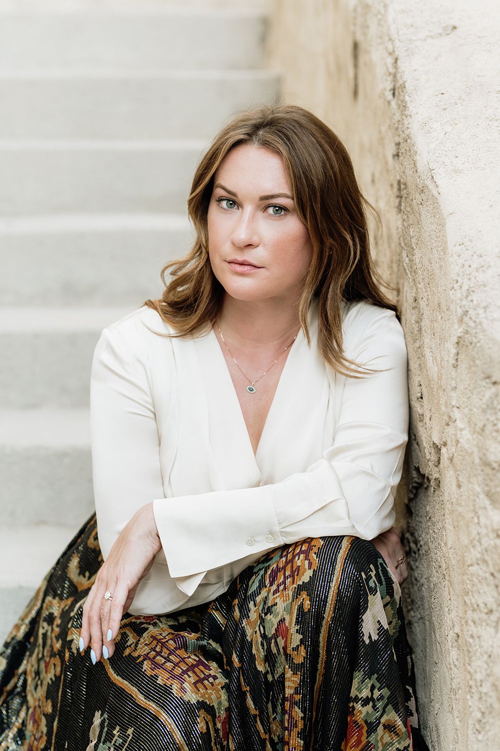 Portrait against stone wall wearing white blouse and patterned skirt.