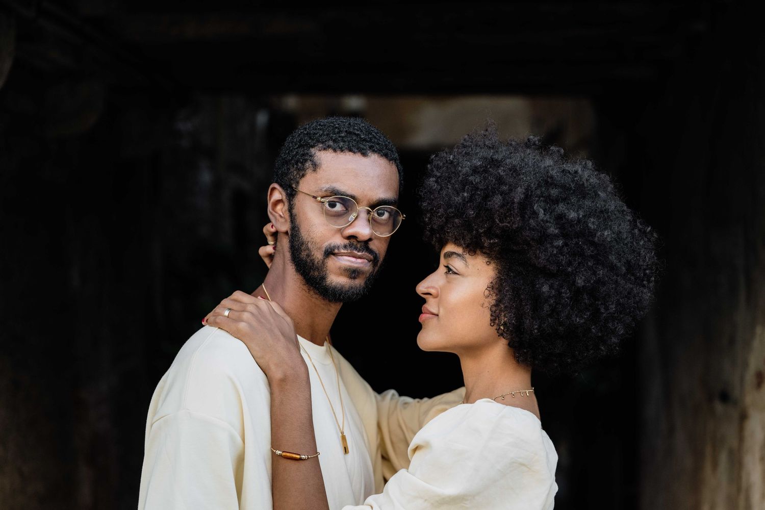 Romantic couple in white outfits sharing tender moments against dark backdrop.