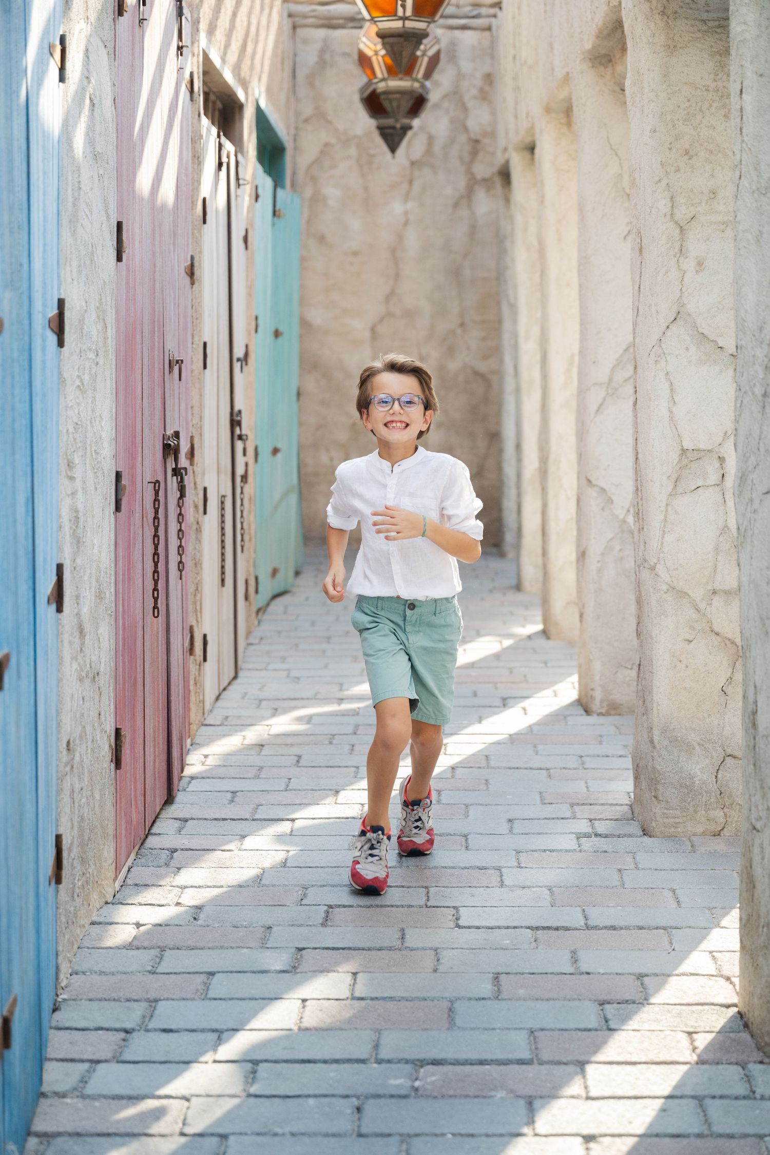 Child running through stone hallway with colorful doors and lanterns.