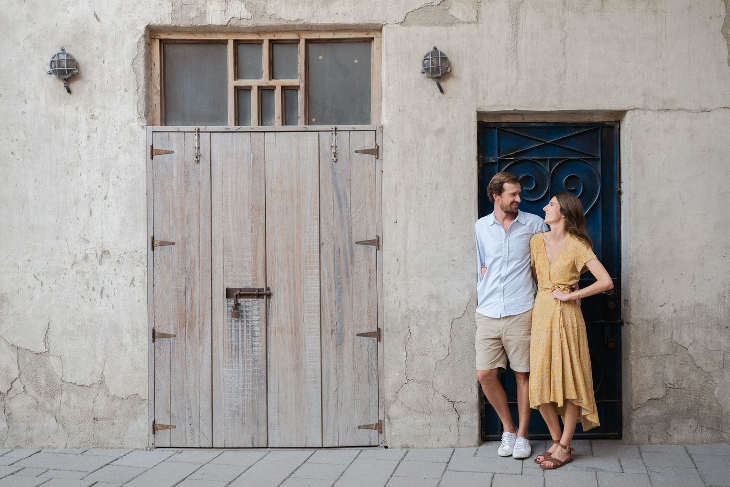 Two people standing by rustic wall and wooden door in casual poses.