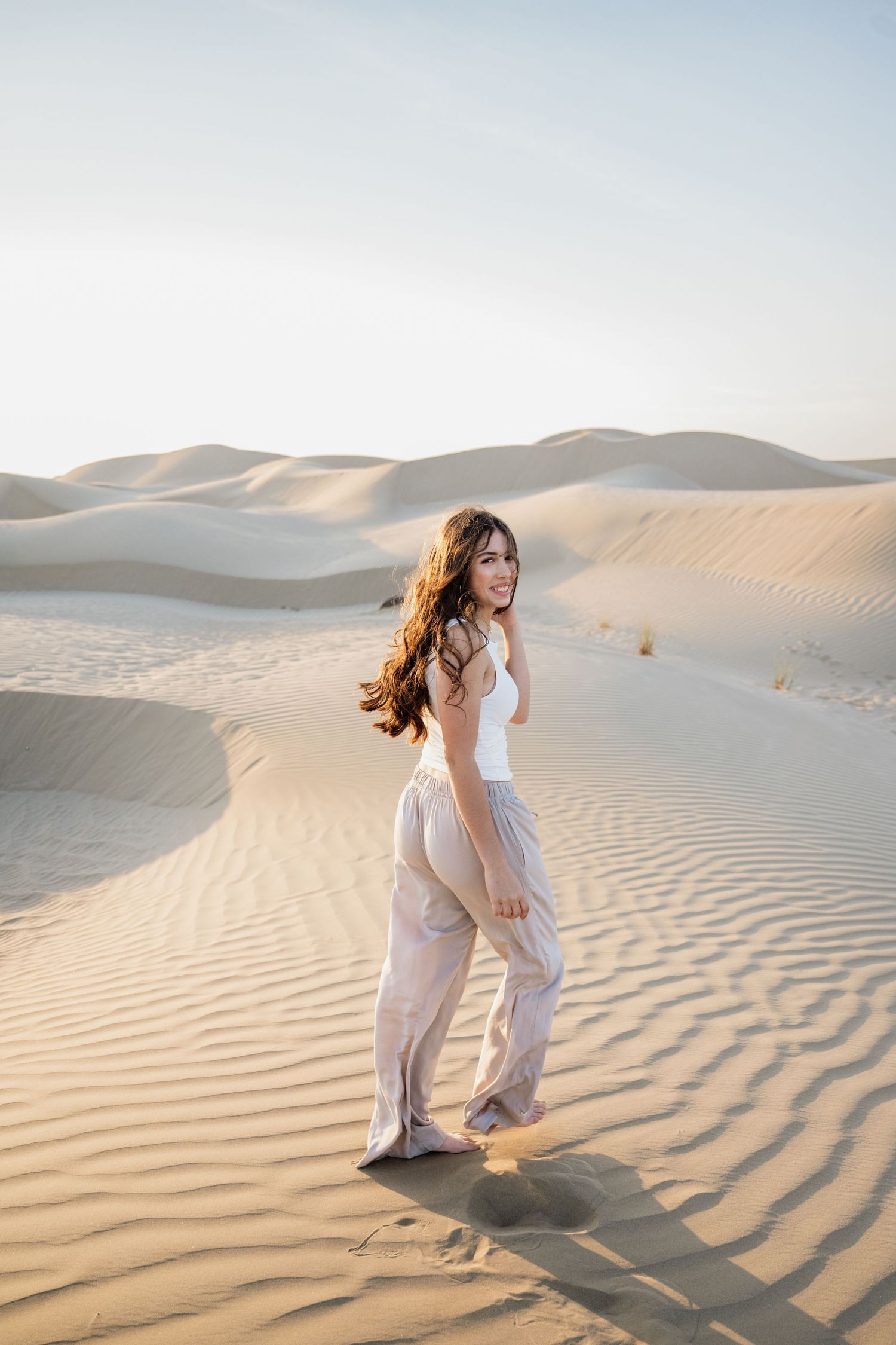 Person in flowing white outfit dancing across desert sand dunes at sunset.