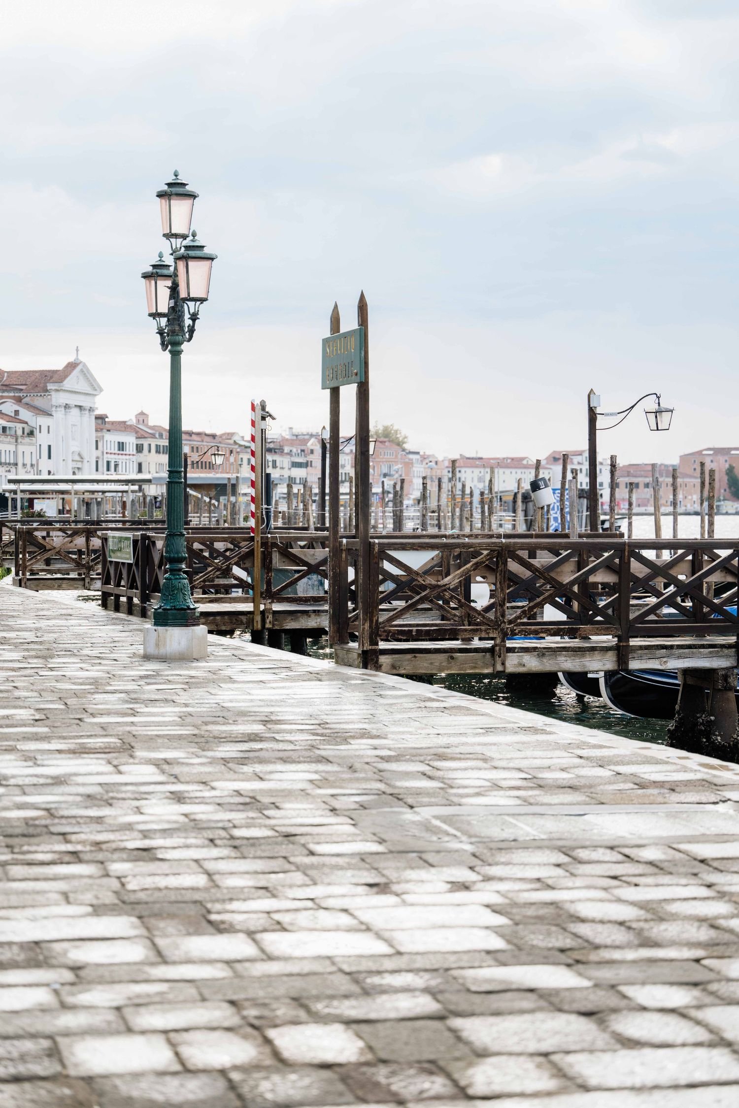 Stone paved walkway along Venice's waterfront with traditional lamp posts and wooden mooring poles.