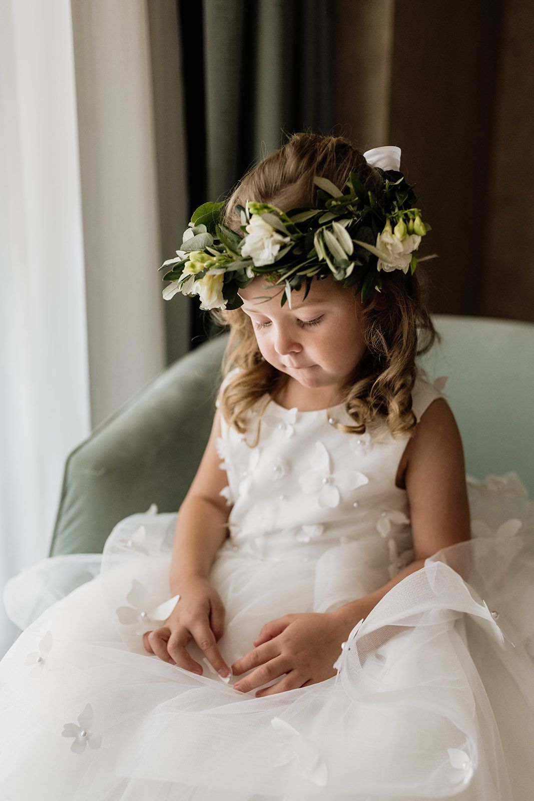 Young attendant in white dress with floral crown sitting gracefully.