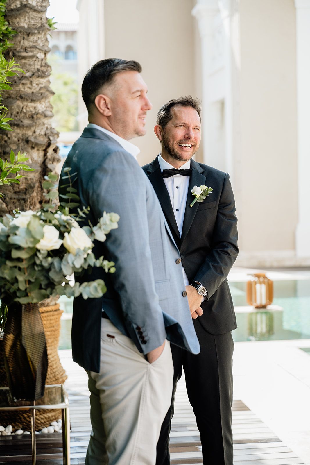Wedding party members in formal attire sharing a candid moment on a covered patio.