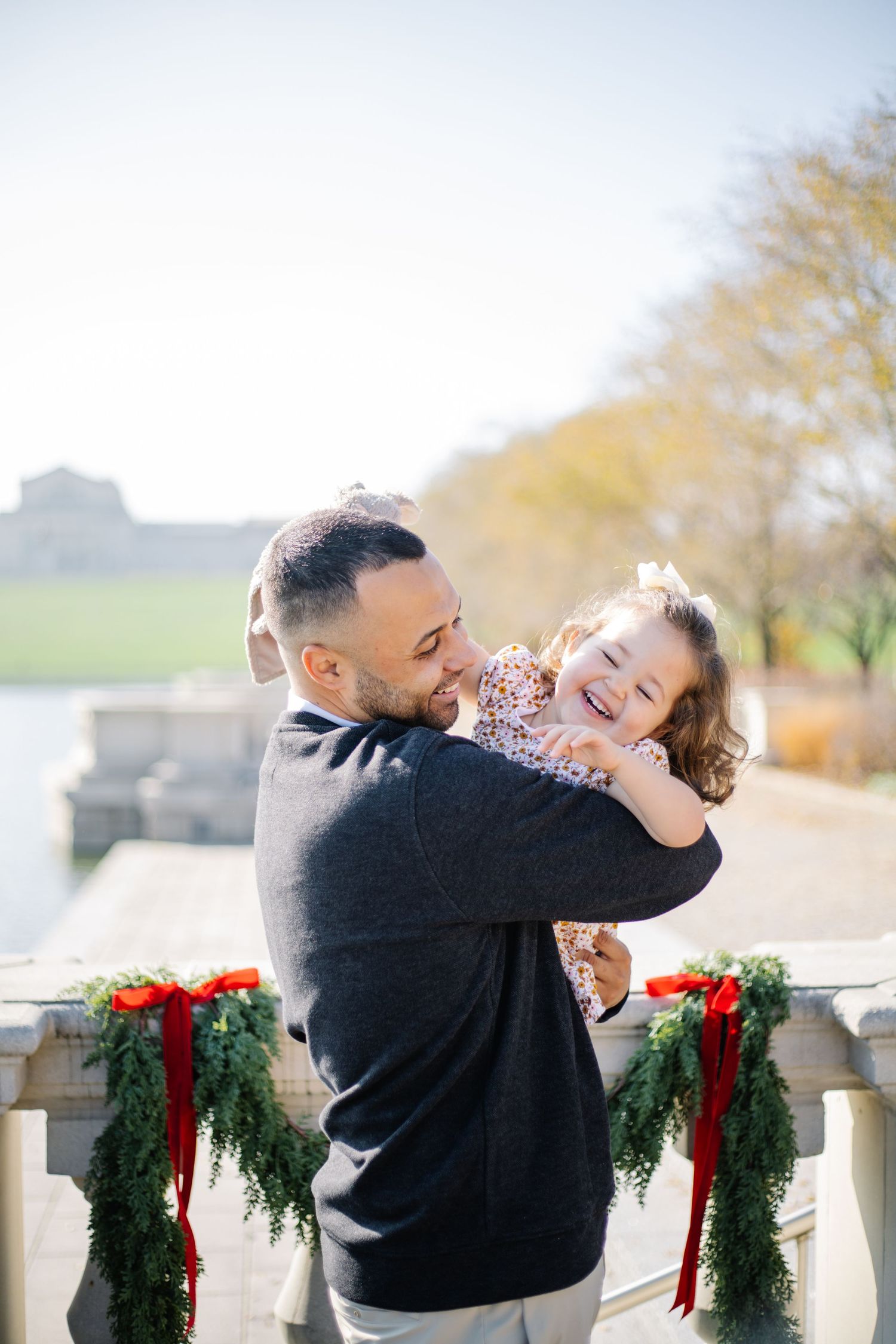 Playful family moments captured on a balcony decorated with festive wreaths and red bows.