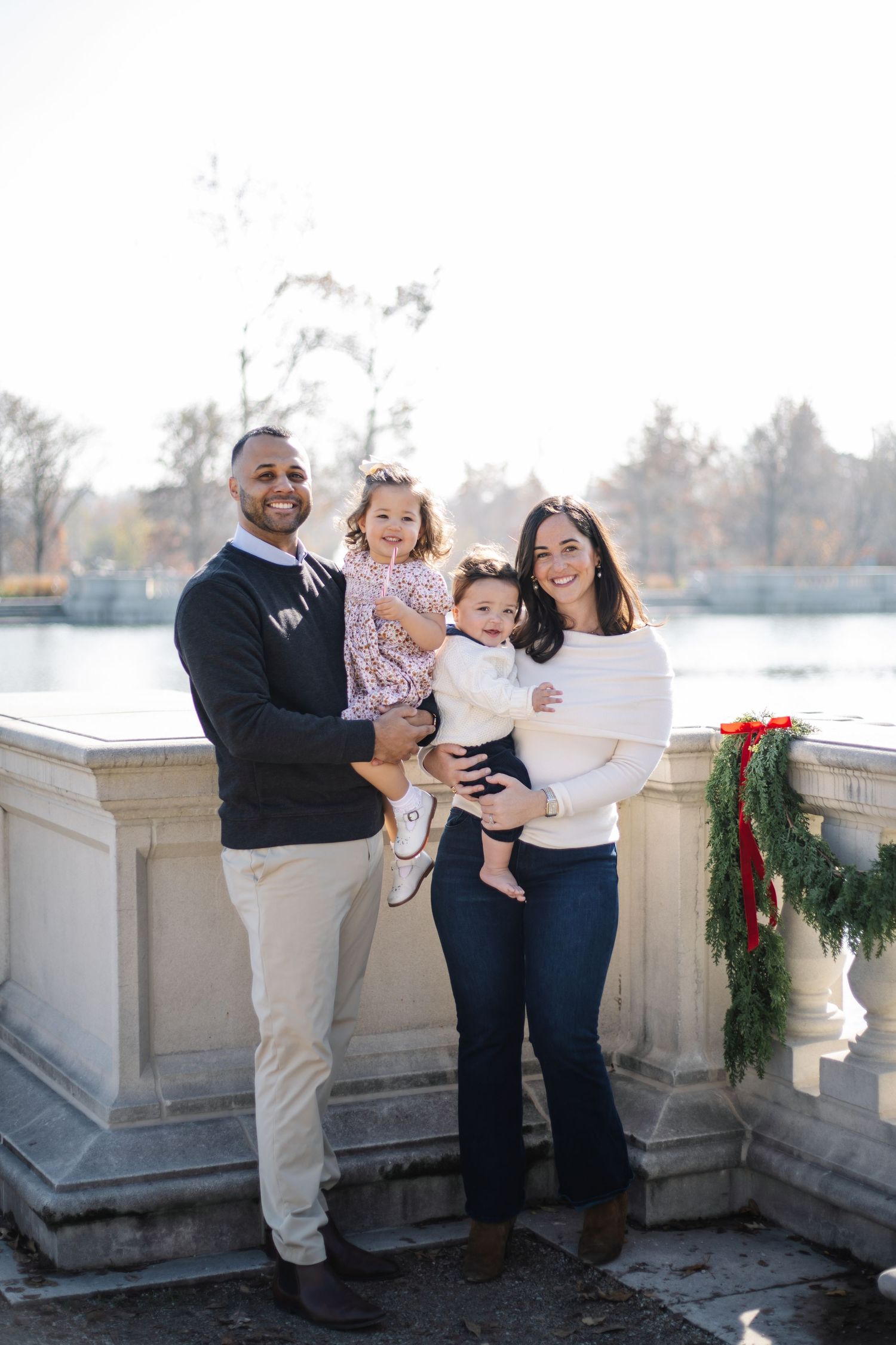 Family portrait session on a stone terrace with holiday decorations and a waterfront backdrop.