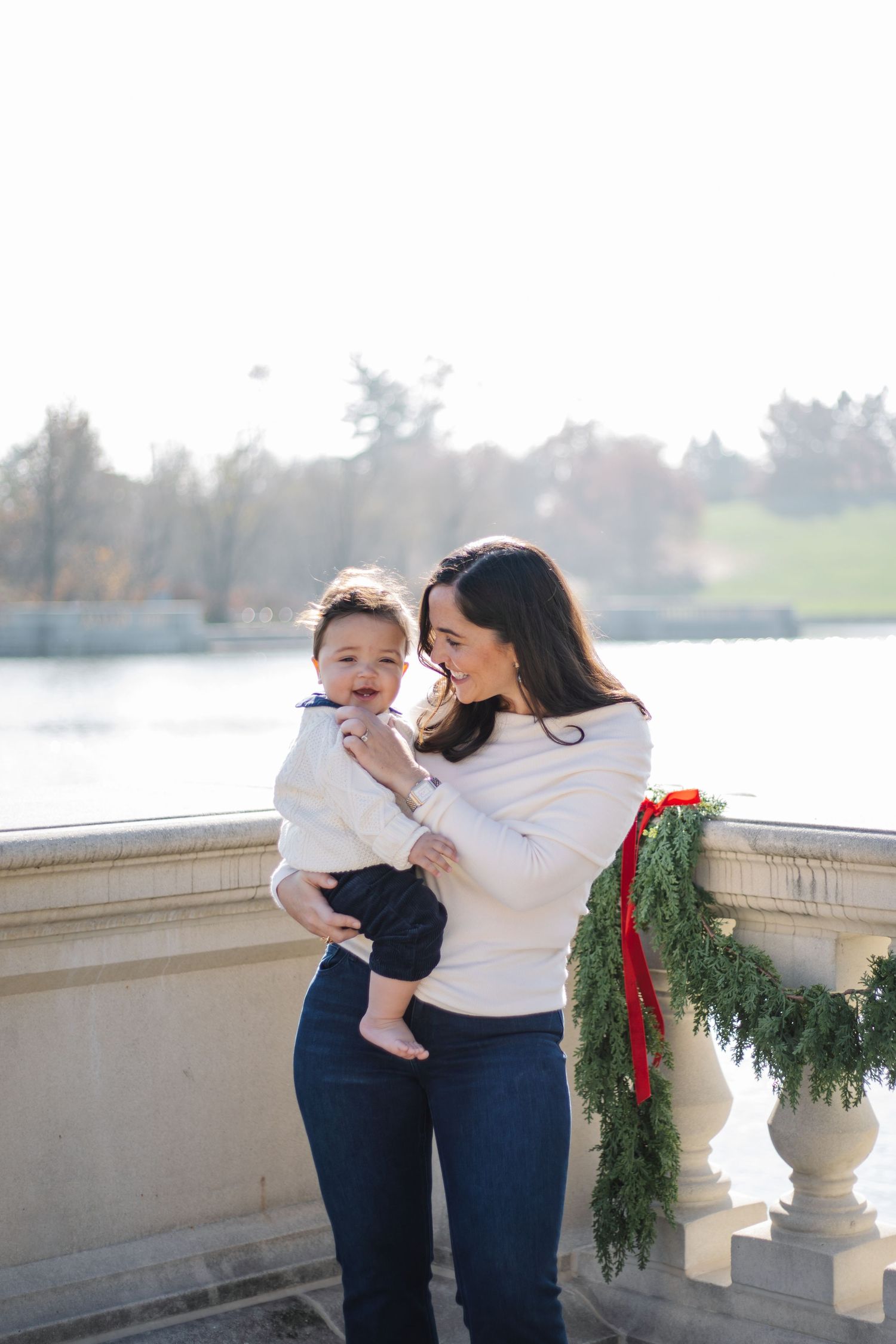 Sweet candid moment between parent and child against lakeside backdrop with winter greenery.