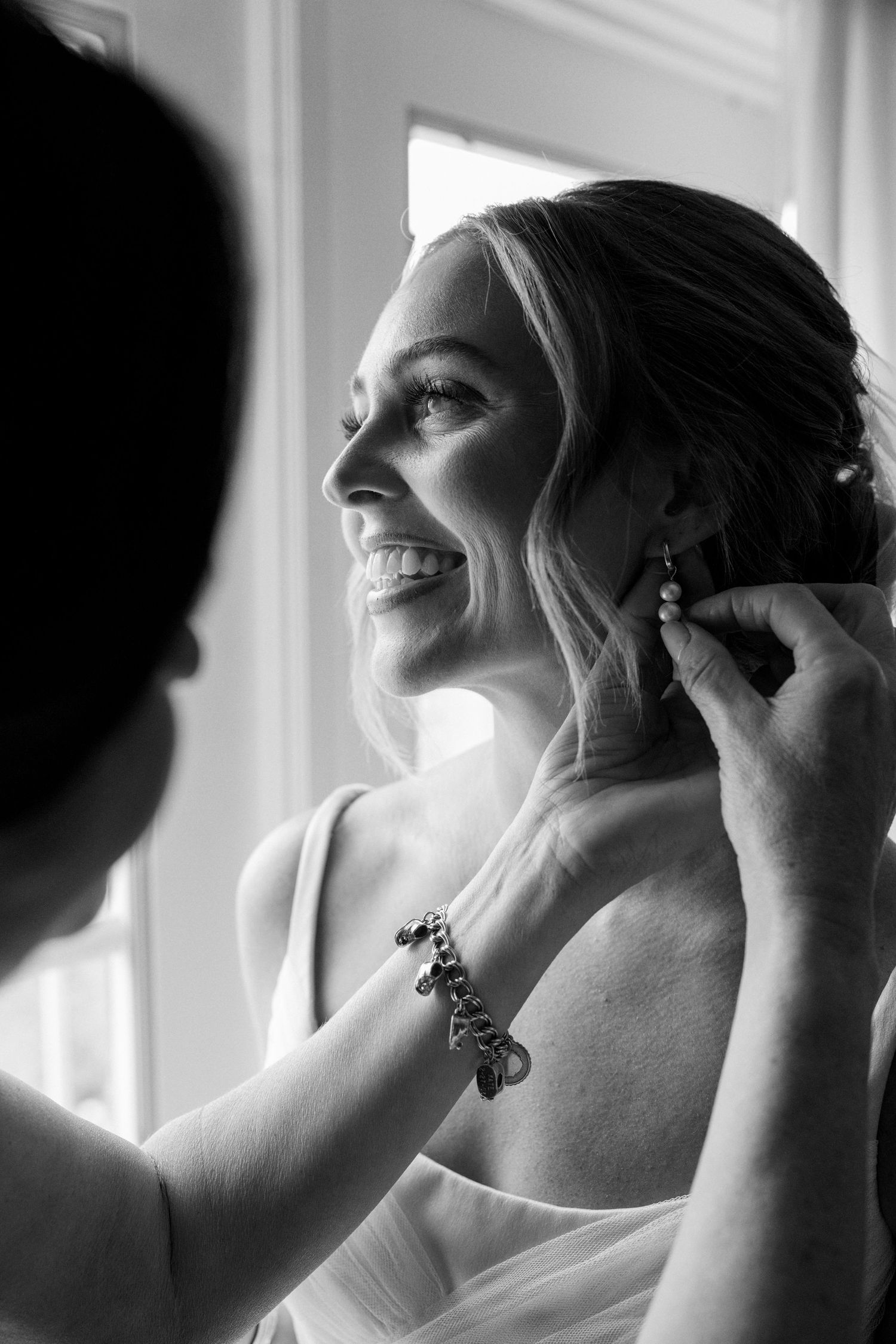 A sequence of black and white photos showing someone putting on elegant drop earrings in natural window light.