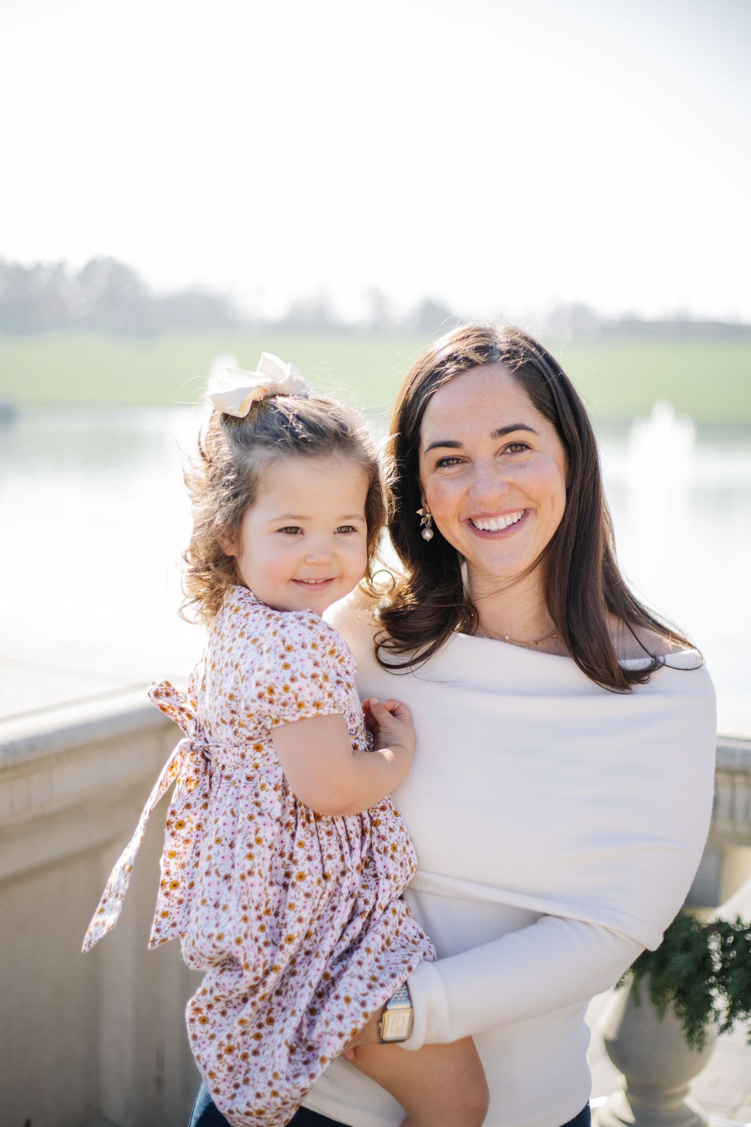 A sweet outdoor portrait of a parent and child in white and floral dress against a bright background.