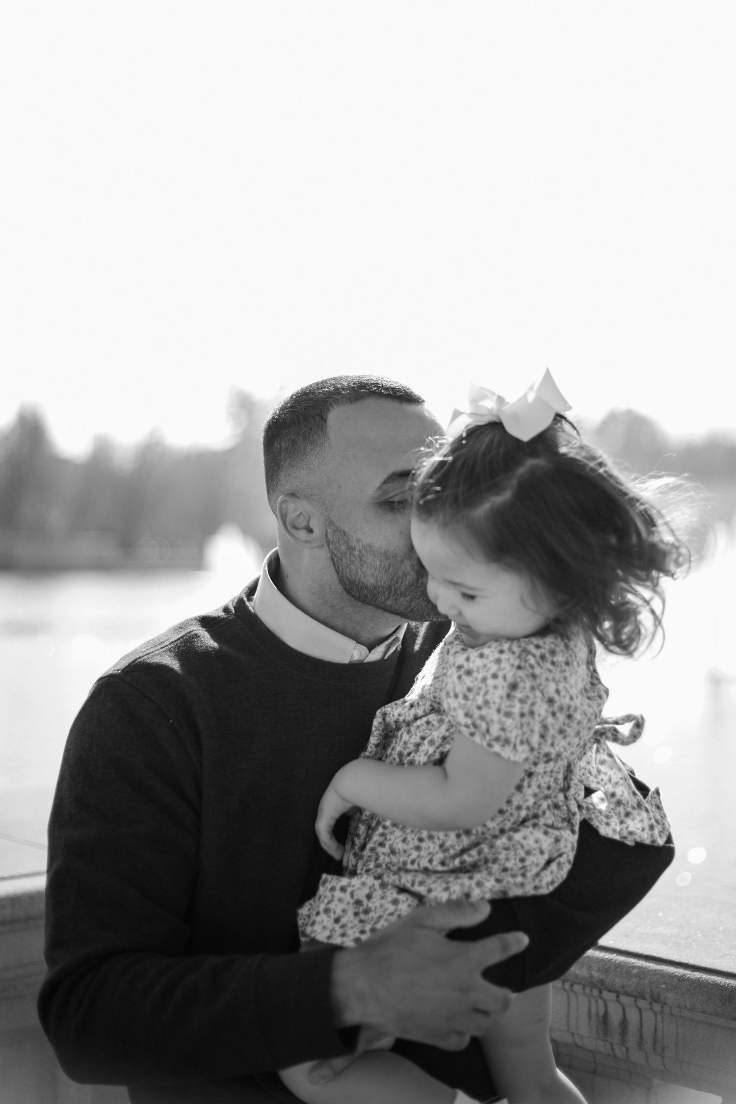 Black and white portrait of tender moment between parent and child against blurred outdoor background.