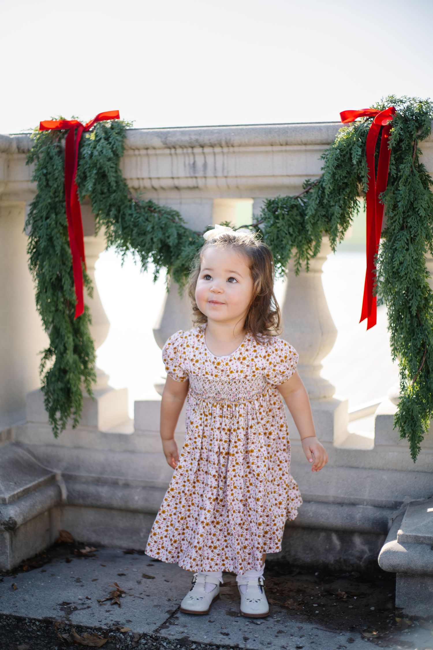 A series of photos showing a small child in a floral dress playing near holiday garland decorations.