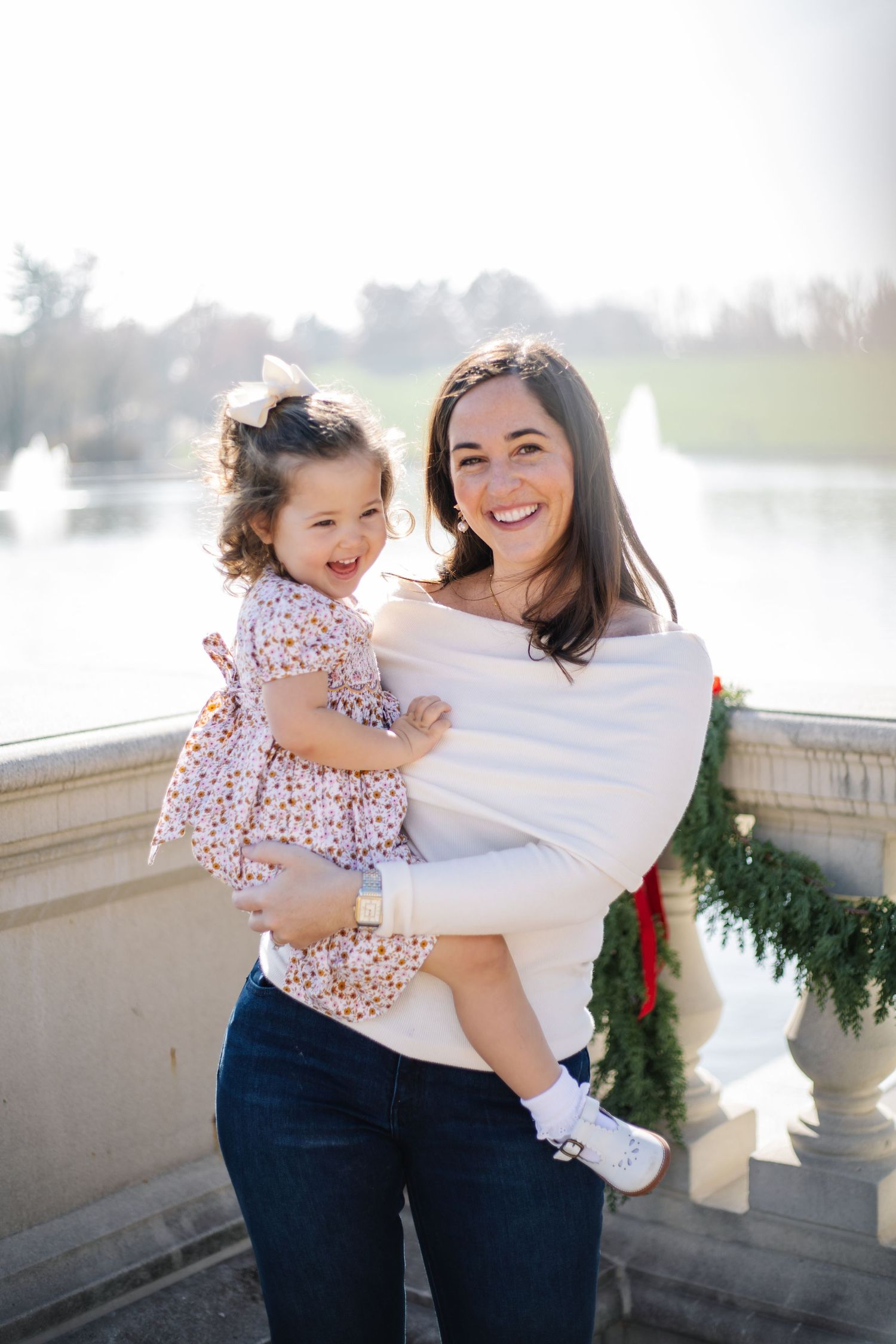 A joyful moment captured in a series of outdoor family photos with decorative holiday greenery in the background.