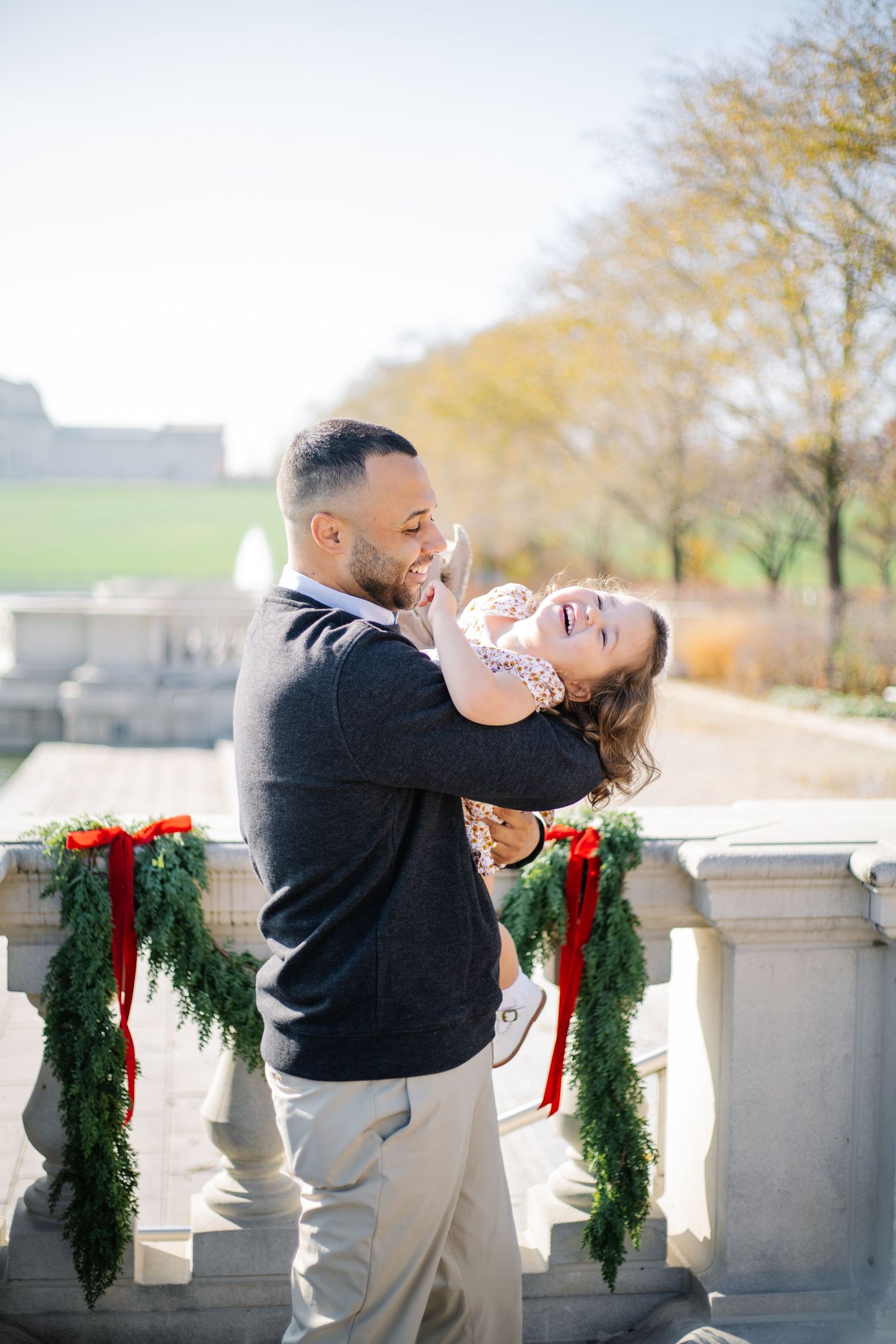 A joyful moment captured outdoors with holiday greenery decorations on stone balustrades in the background.