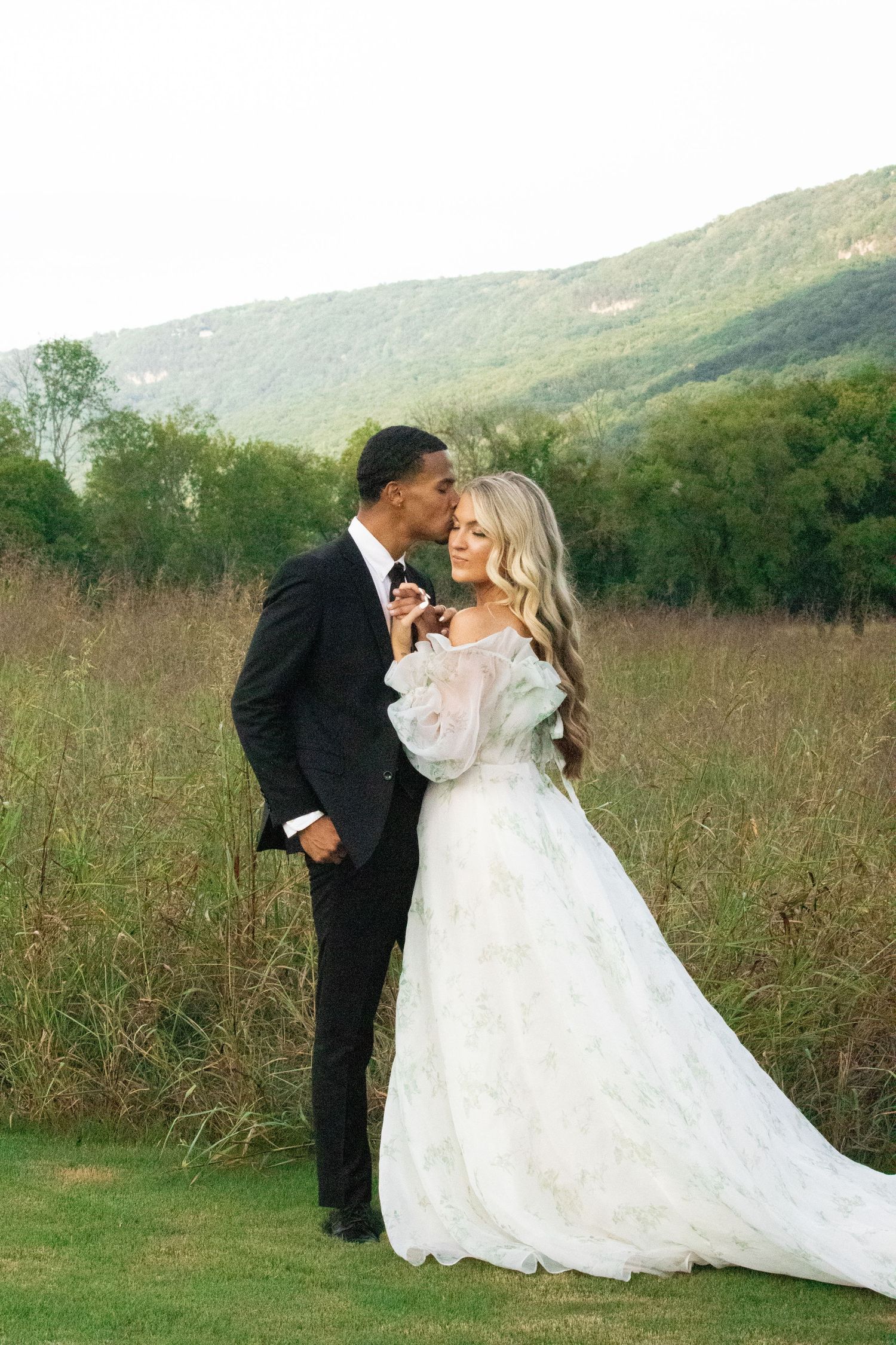 A romantic wedding photoshoot in a rustic field with rolling hills in the background.