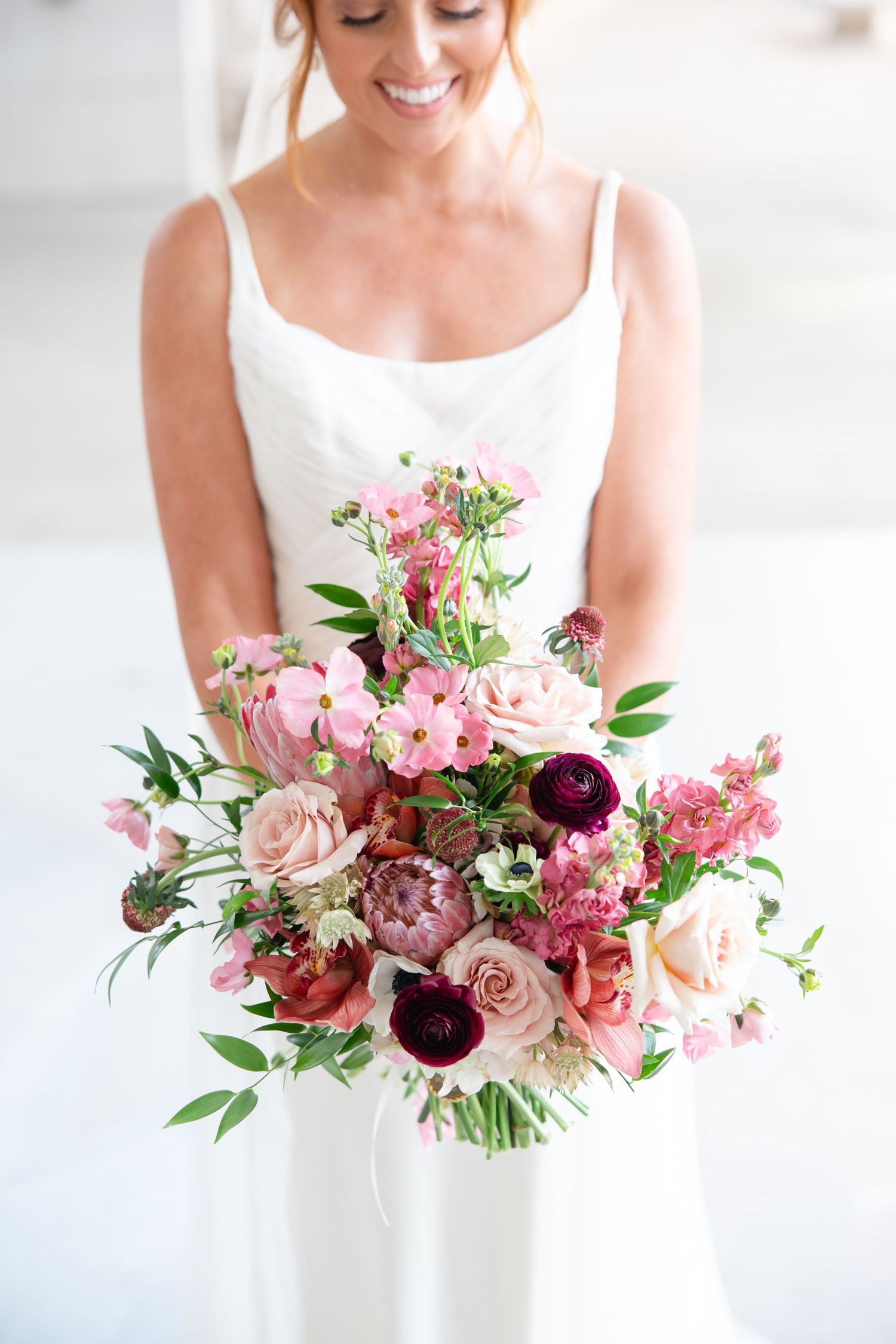 Beautiful bridal bouquet with pink peonies, burgundy dahlias, blush roses and greenery against white wedding dress.