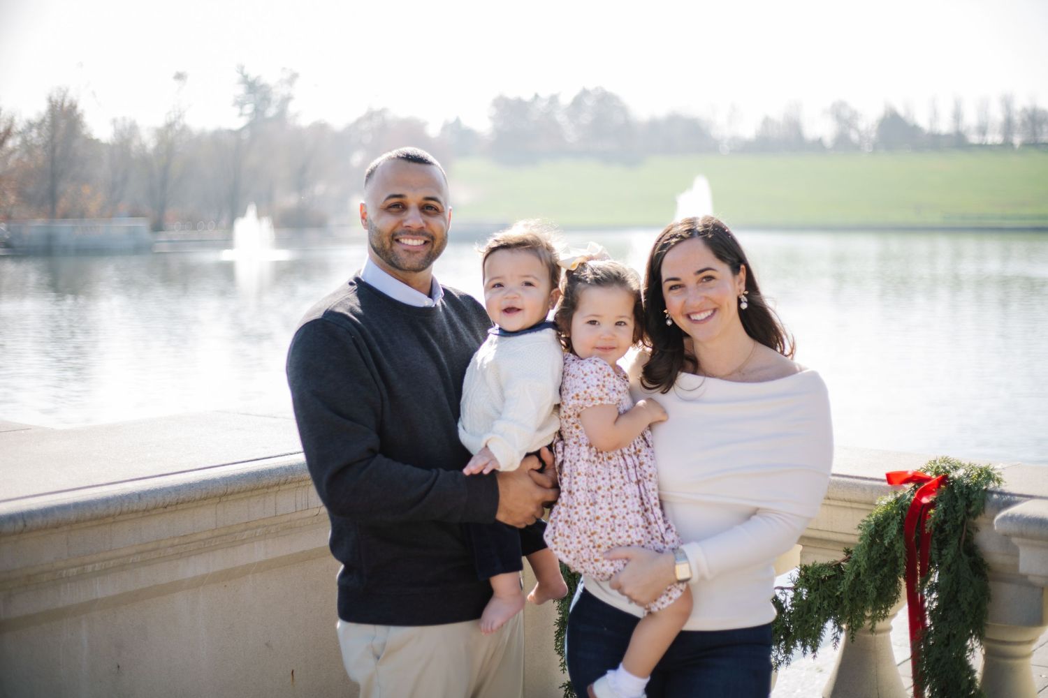 Family enjoying a tender moment together on a stone balcony overlooking a serene lake on an autumn day.