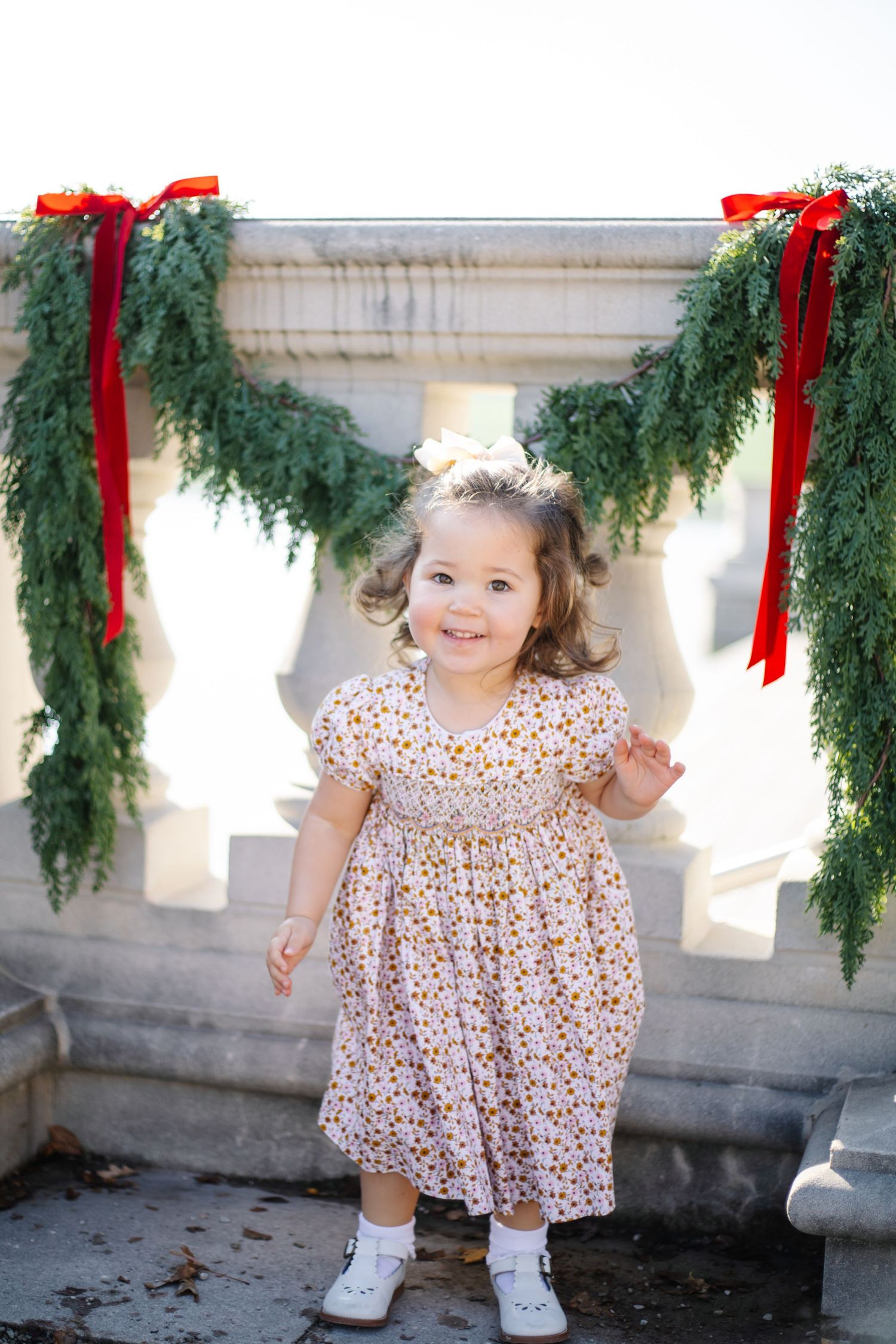 A playful moment captured on a stone terrace with hanging evergreen garlands and red ribbons.