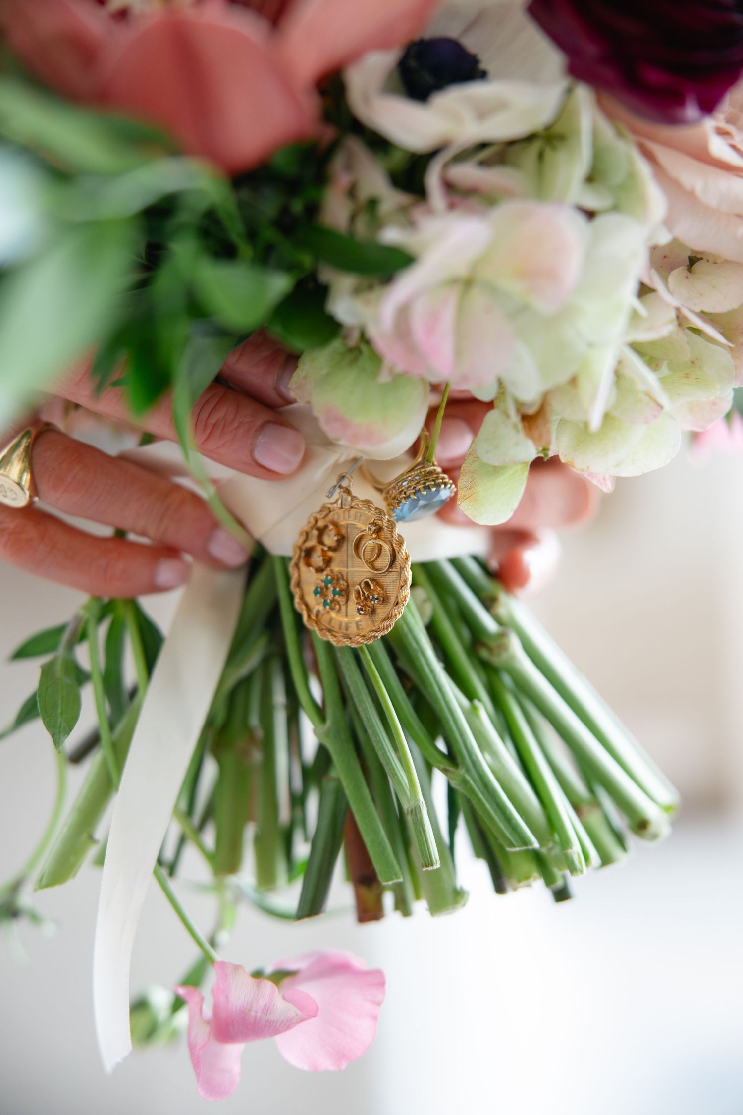 A close-up sequence showing gold charm details being attached to a pink and white floral wedding bouquet.