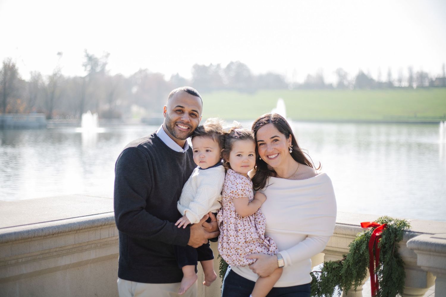 A happy family poses together on a lakeside deck decorated with holiday greenery and red bows.
