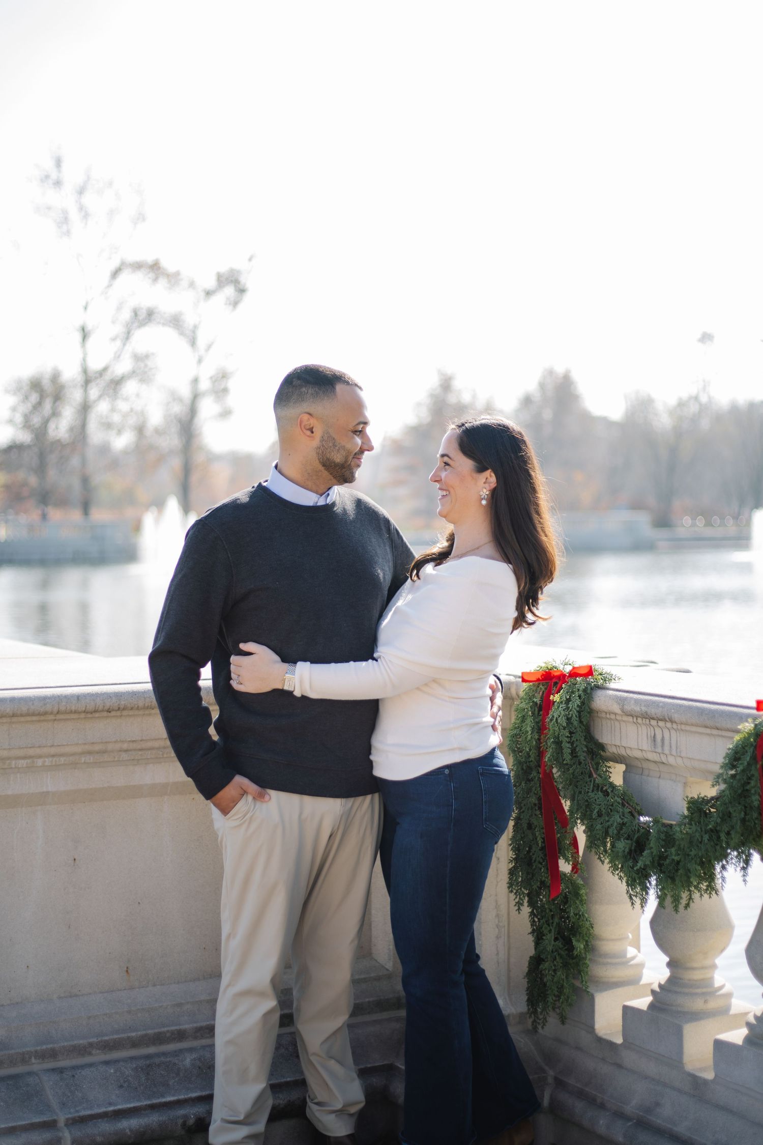 A couple shares romantic moments on a balcony decorated with holiday greenery and red bows.