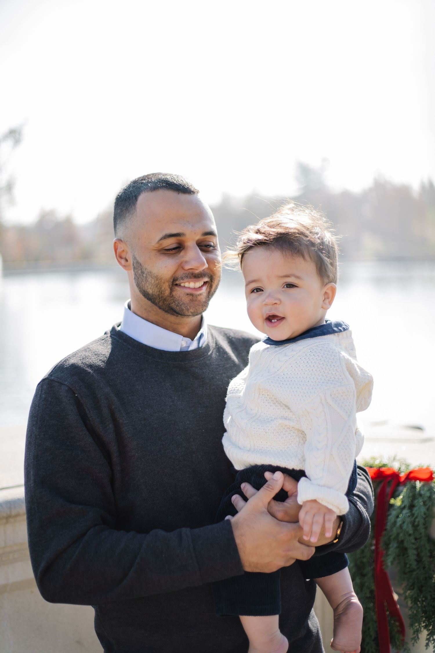 A heartwarming outdoor portrait of parent and child in matching white sweaters by a lake.