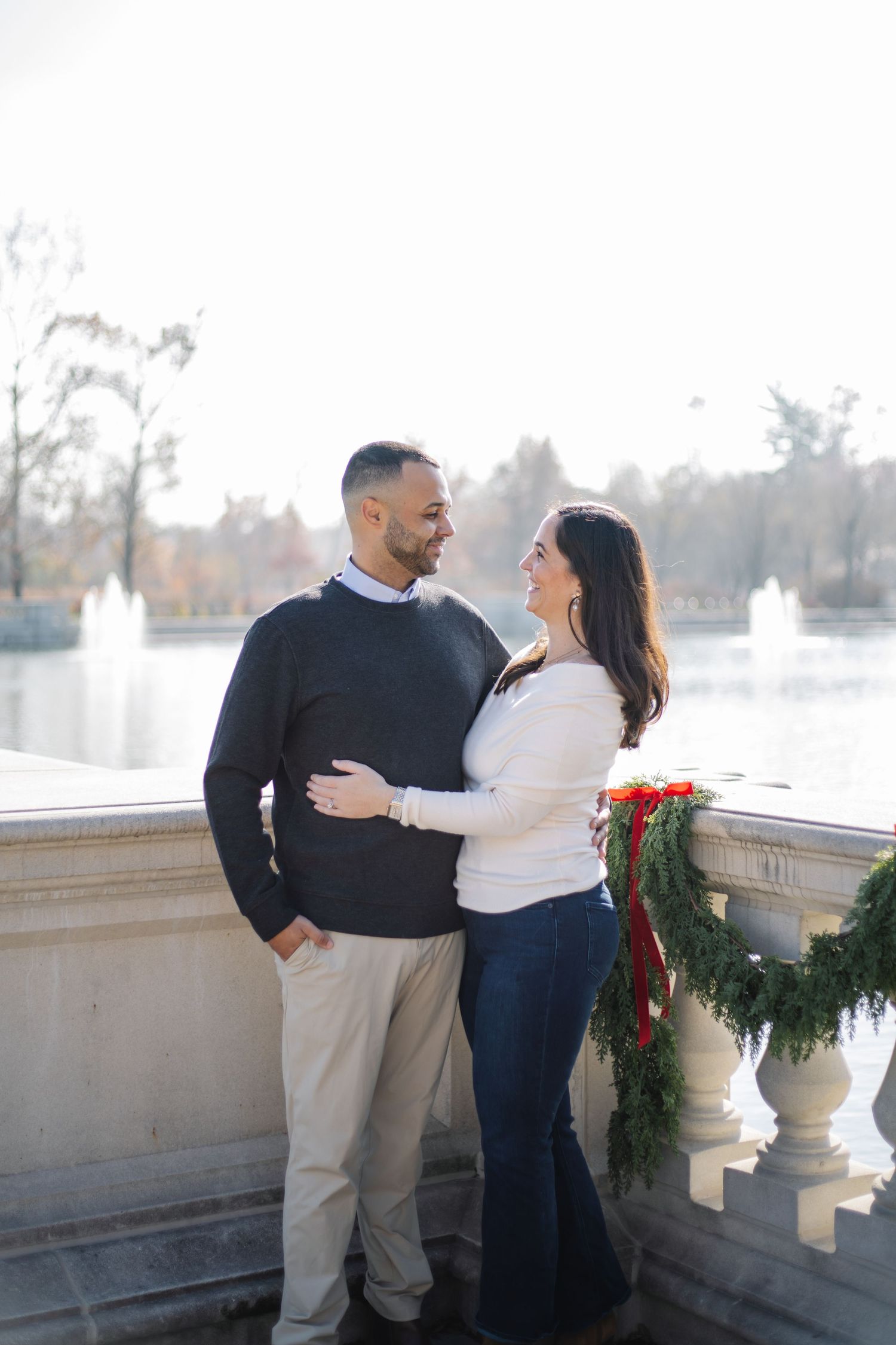 A couple shares intimate moments along a stone balustrade decorated with holiday greenery and red bows.