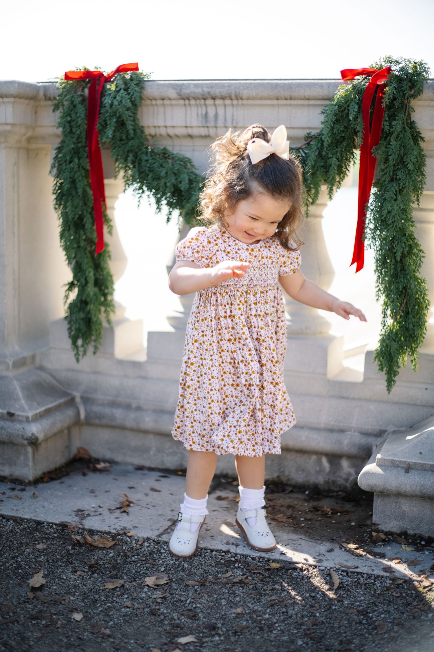 A sequence of playful poses by a toddler in a patterned dress near stone railings with holiday greenery.