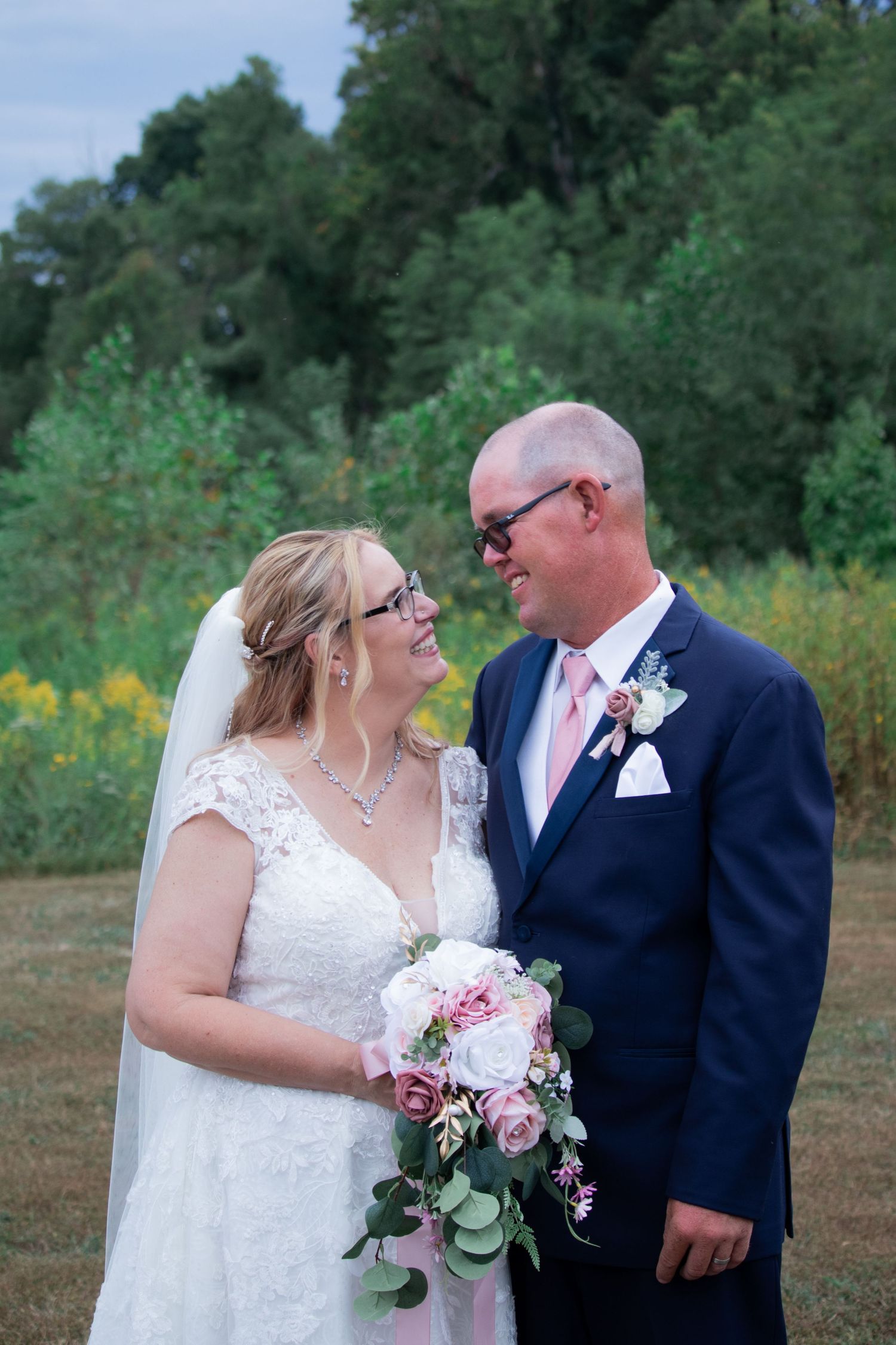 Wedding couple shares intimate moments in an outdoor field with natural greenery.
