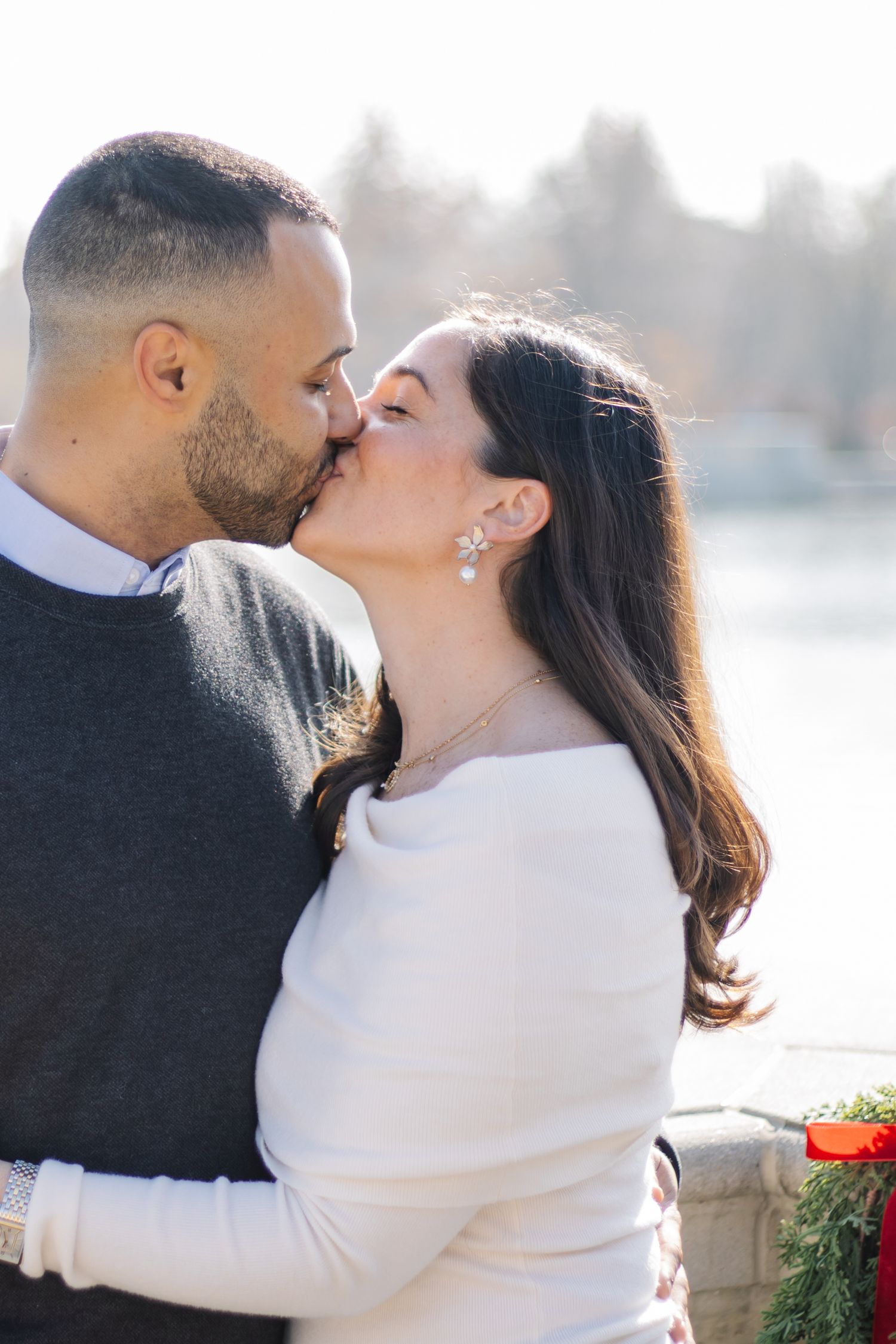 A romantic couple shares a tender kiss in front of a waterfront view on a misty winter day.