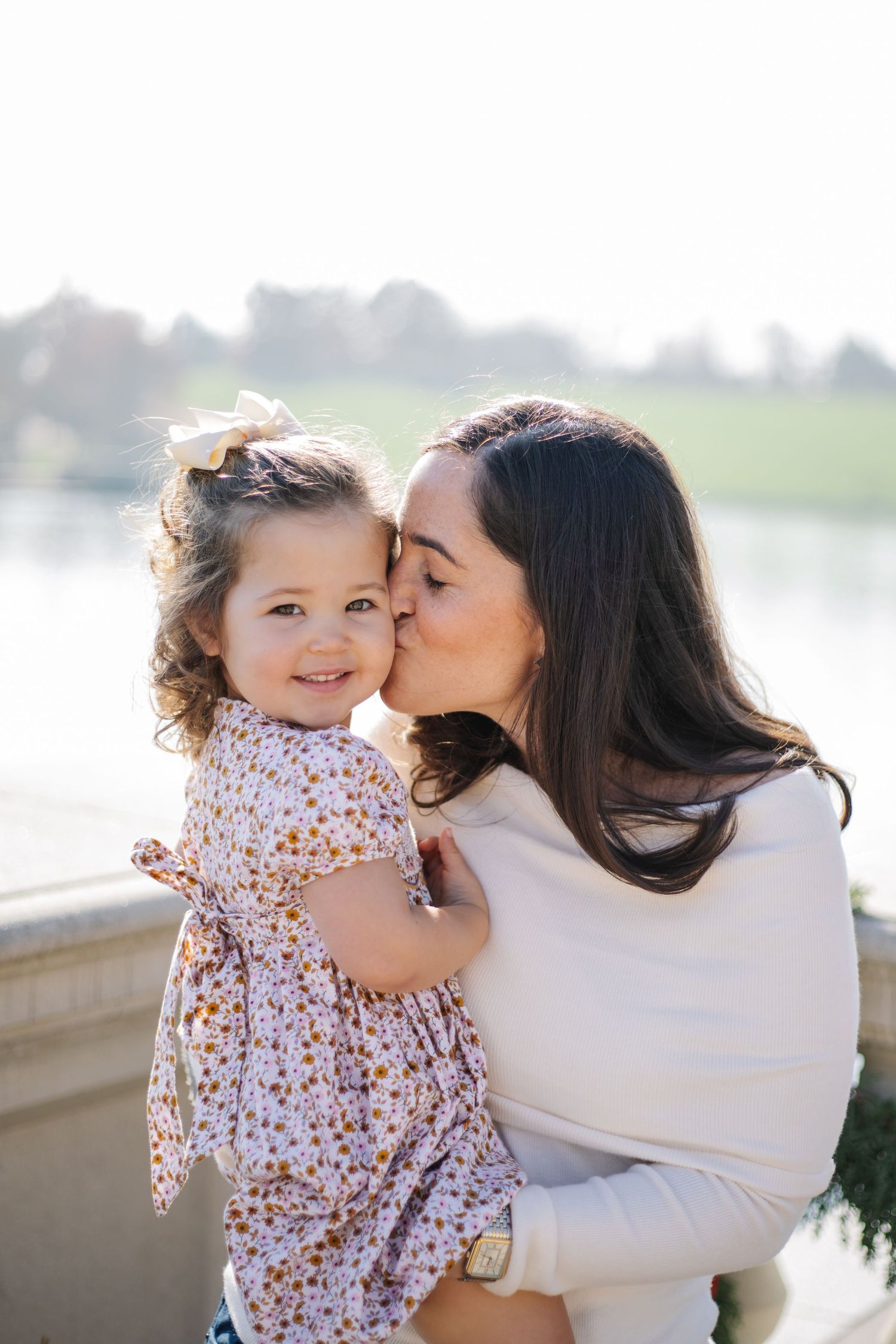 A tender moment between parent and child in floral dress against a waterfront backdrop during golden hour.