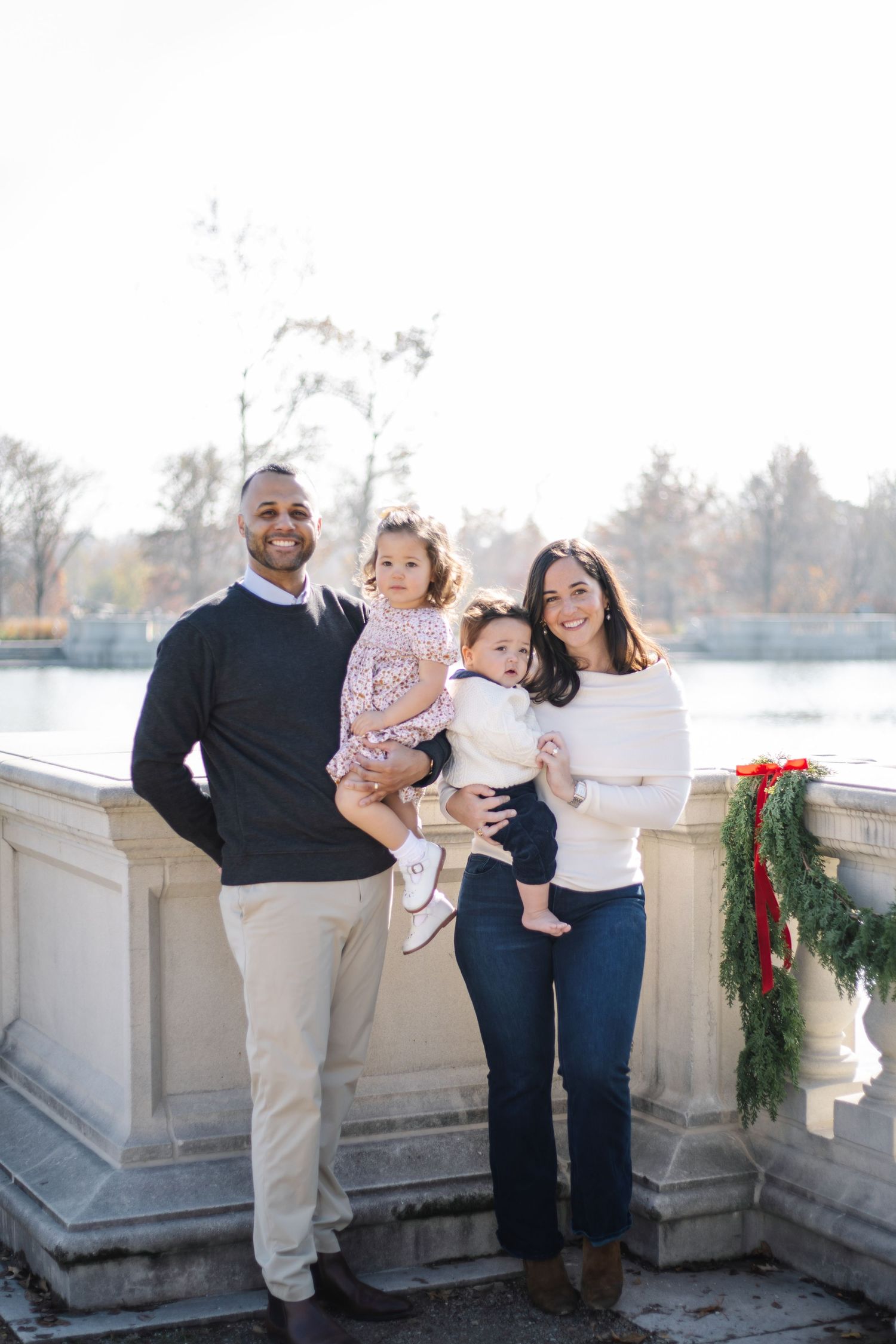 A happy family shares tender moments together during an outdoor winter photoshoot near a decorated stone railing.