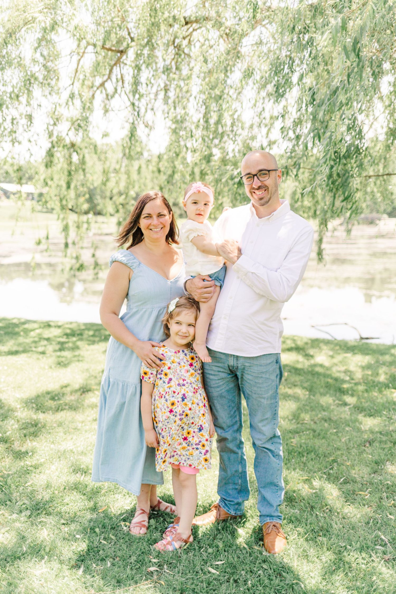 Family of four dressed in blues, whites and florals smiling under a willow tree during a family session in the hudson Valley of NY
