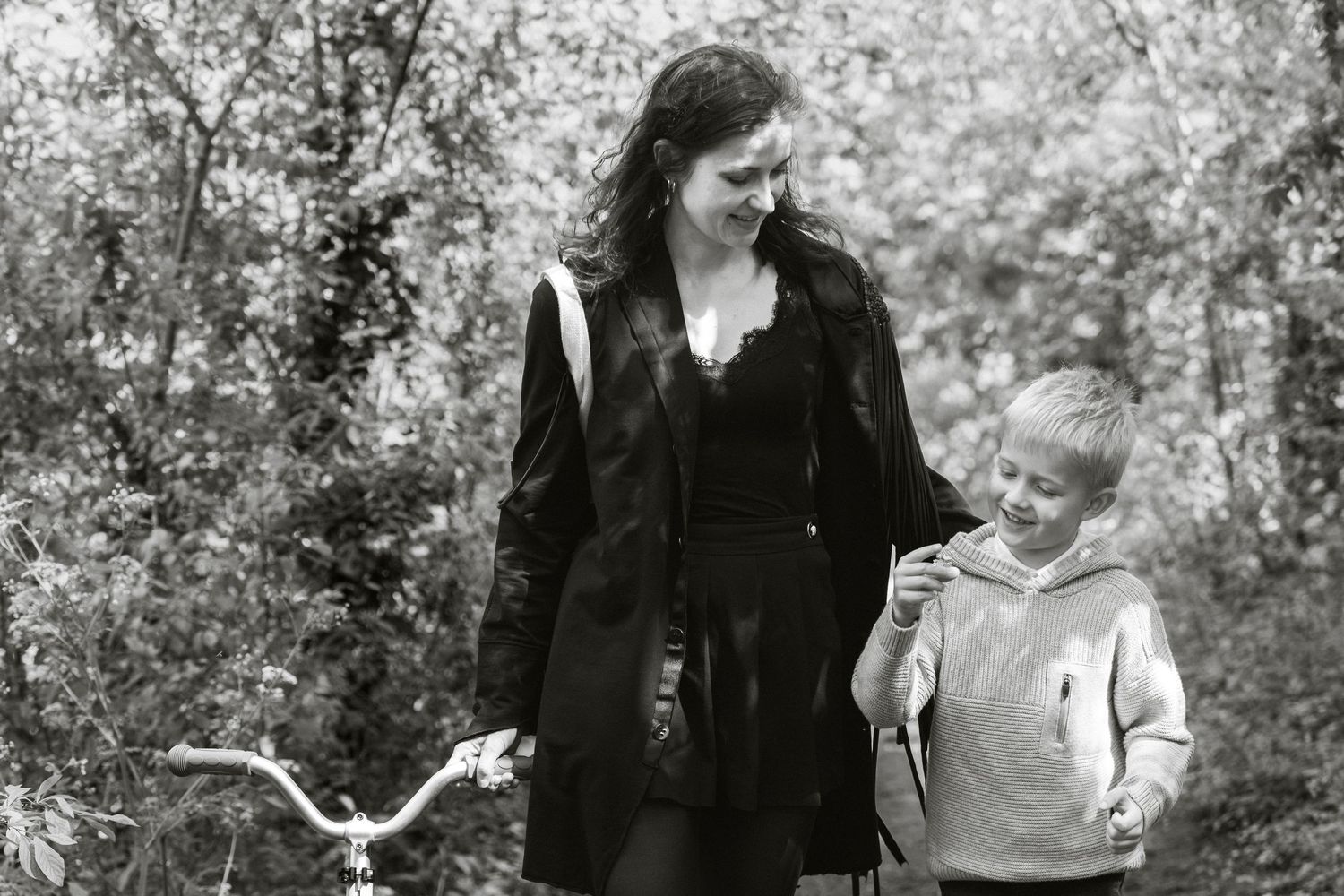 Woman and young boy walking together on a forest path with a bicycle in black and white photo.