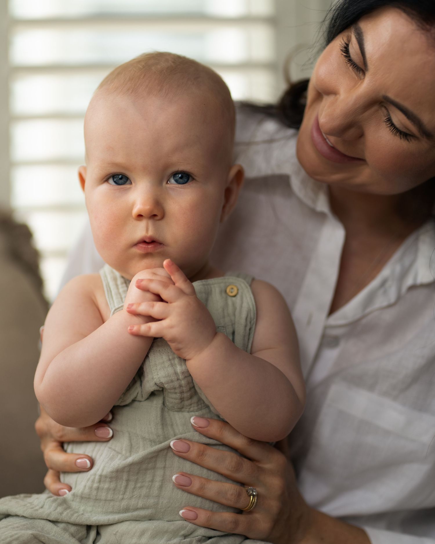 Baby in mint green romper being held near a sunny window.