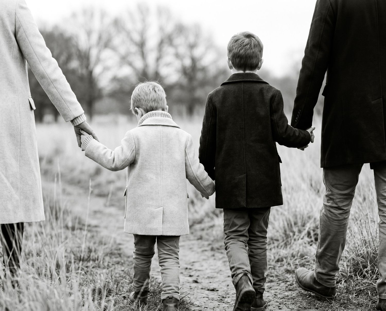 Black and white photo of a family with two children holding hands walking along a rural path outdoors.