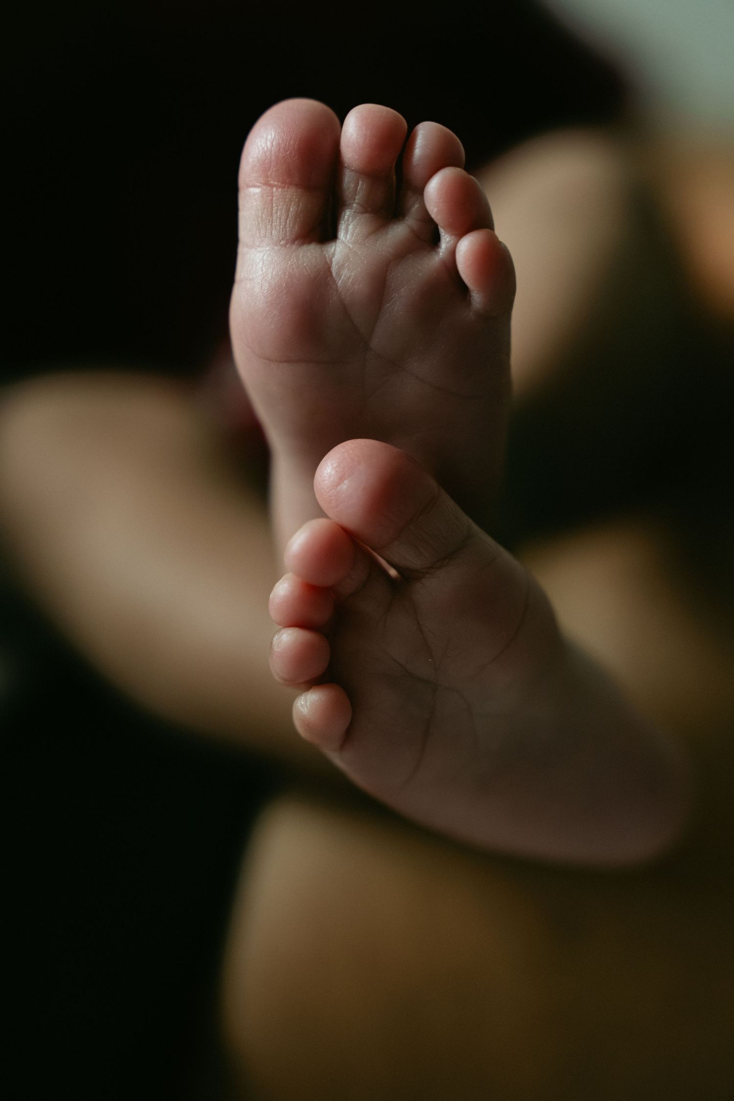 Close-up of tiny newborn baby feet with soft pink toes against a dark background.