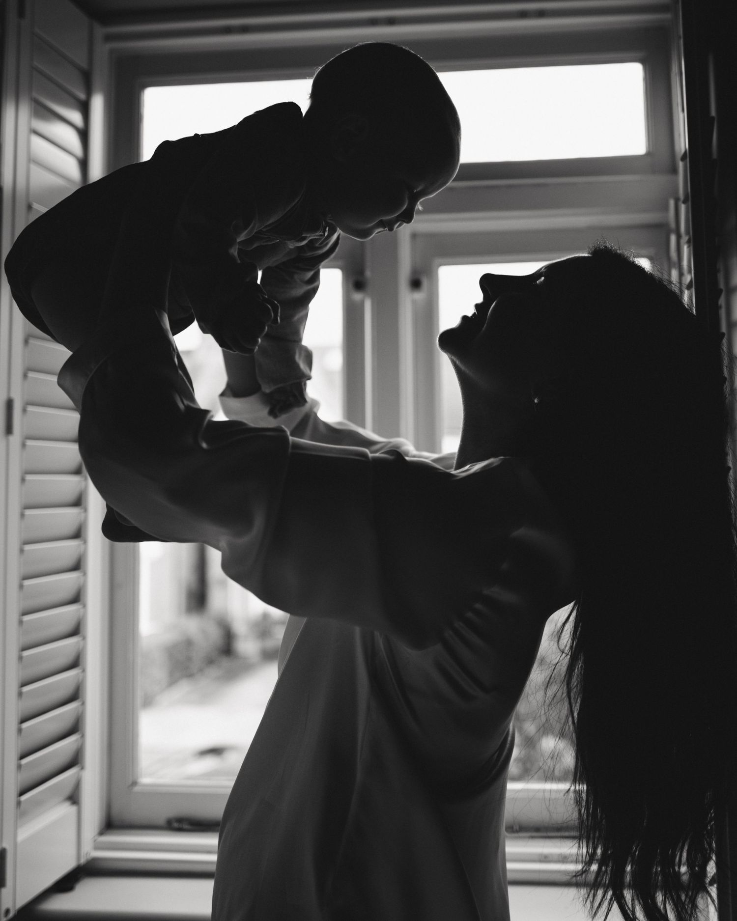 A silhouetted figure lifting a small child against a bright window backdrop.