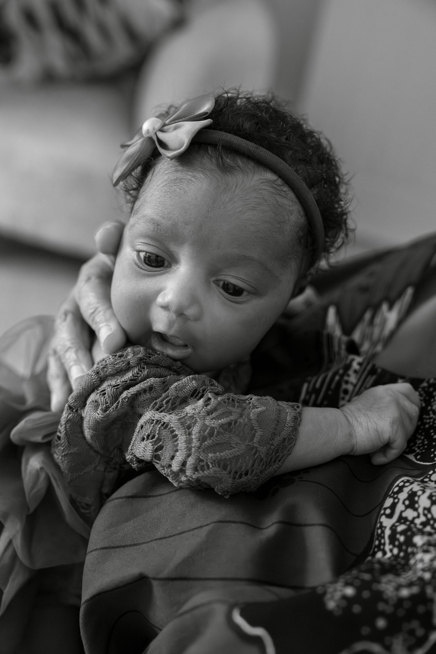 Black and white photo of a newborn baby girl with a bow headband being cradled in loving arms.