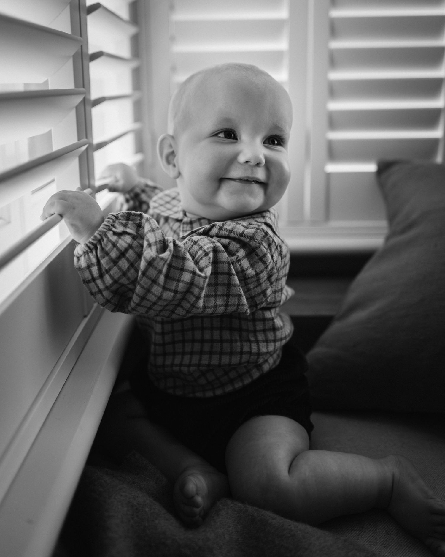 Black and white photo sequence showing a baby in plaid shirt smiling and moving on a couch.